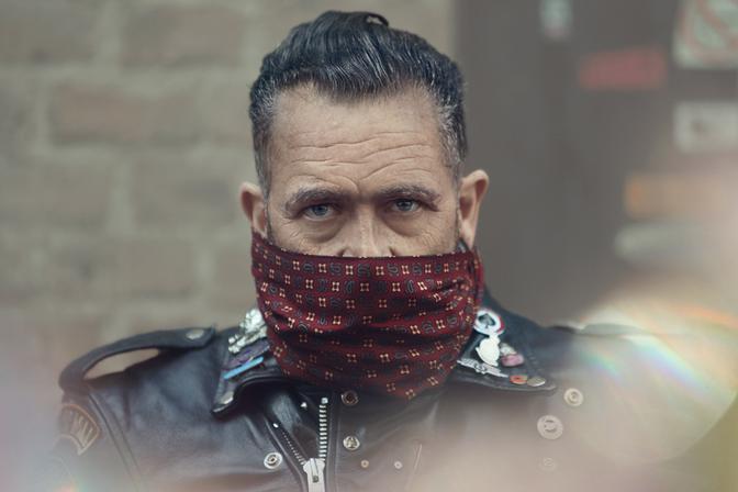 A man with a leather jacket and a bandana covering his face, wearing a motorcycle helmet and riding a motorcycle.