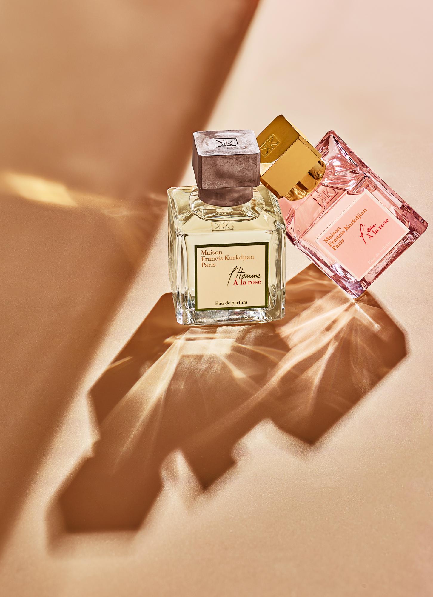 Two perfume bottles, one clear and one pink, with gold caps and labels featuring the name 'Maison Francis Kurkijian' and 'L'Homme à la Rose' and 'Fleur' respectively.