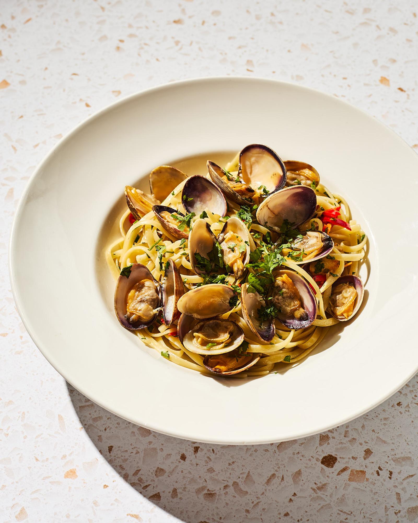 A plate of linguine with clams, garnished with parsley and red peppers, served on a white plate.