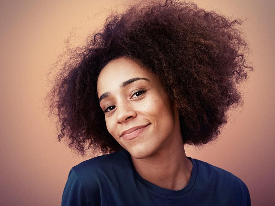 A young woman with curly, dark brown hair and a warm, gentle smile, wearing a blue t-shirt.