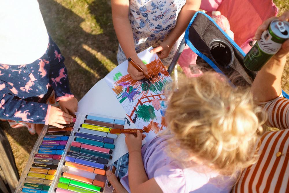 A group of children are gathered around a table, each holding a marker and creating a colorful drawing. The atmosphere is playful and creative, with a sense of fun and energy.