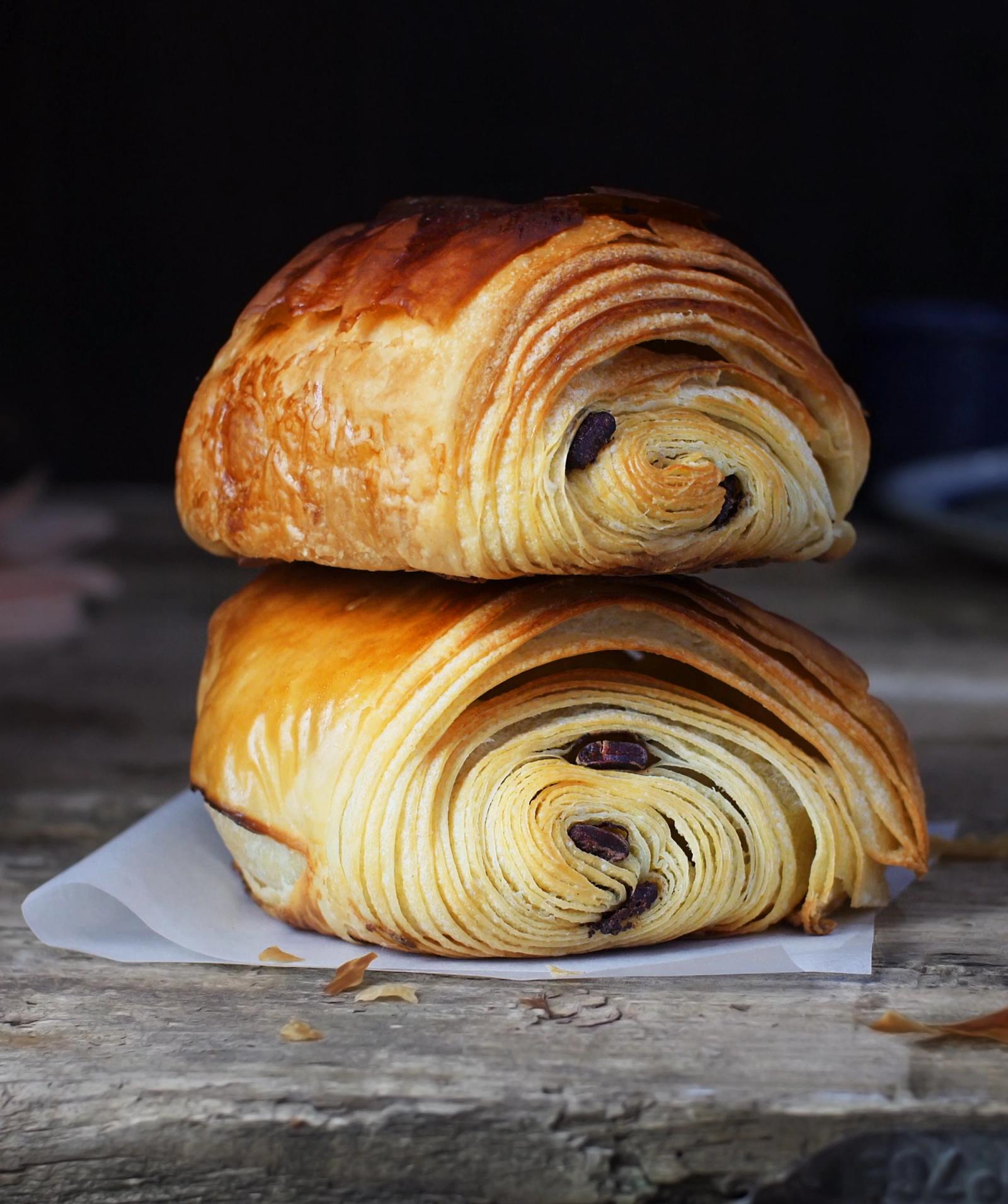A stack of two golden-brown, flaky, and crispy croissants, one on top of the other, with a dark chocolate filling visible through the layers.