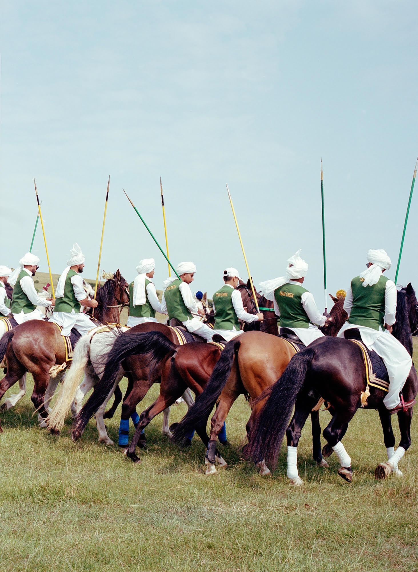 A group of men on horseback, wearing green and white clothing, with long spears, in a grassy field.