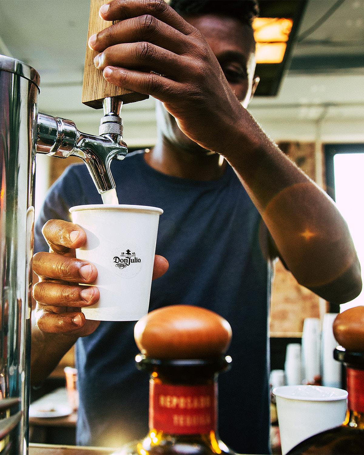 A barista pouring a drink from a coffee machine into a cup with the logo 'Don Julio' on it.