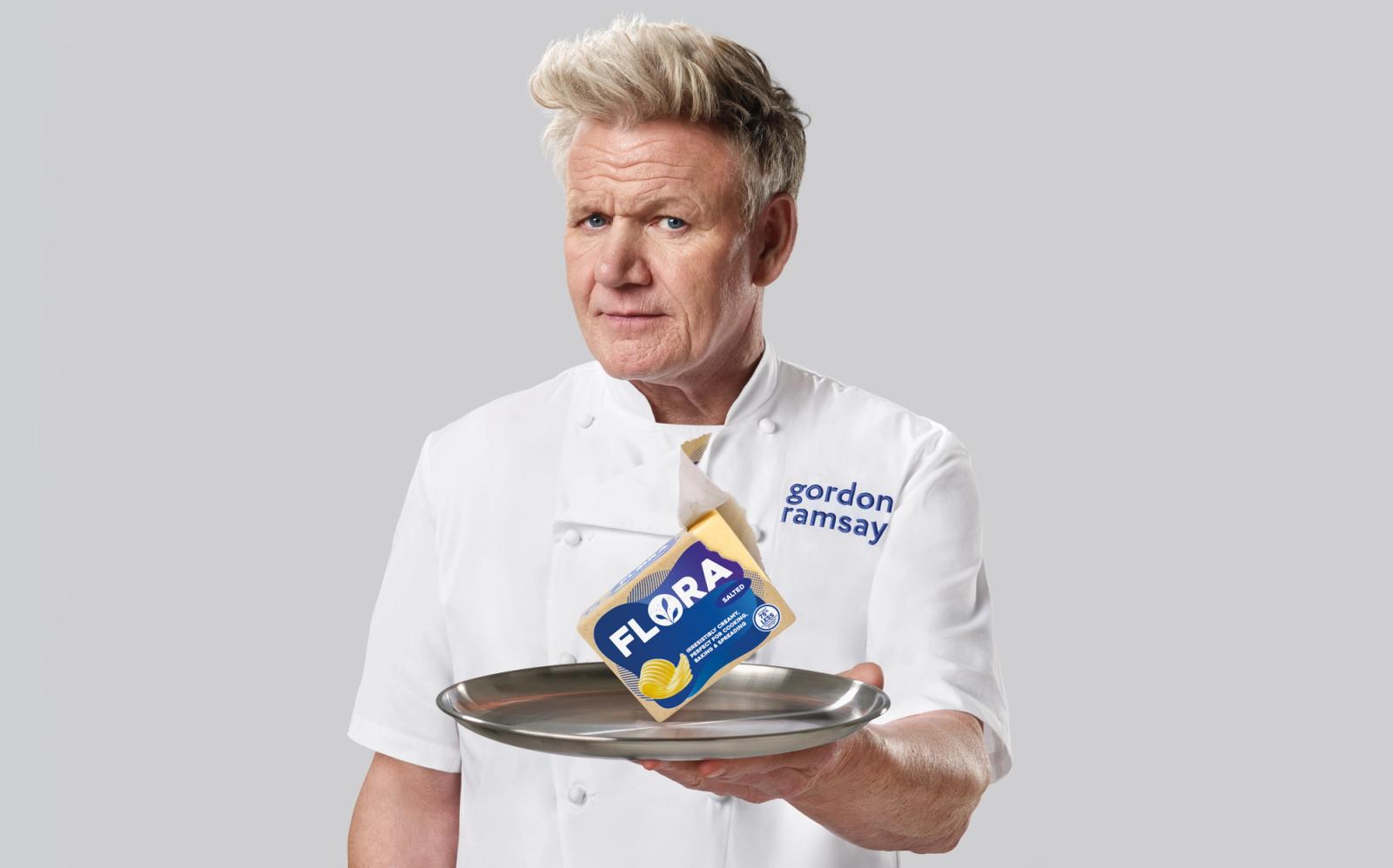 A person holding a block of butter on a silver tray, wearing a white chef's coat.