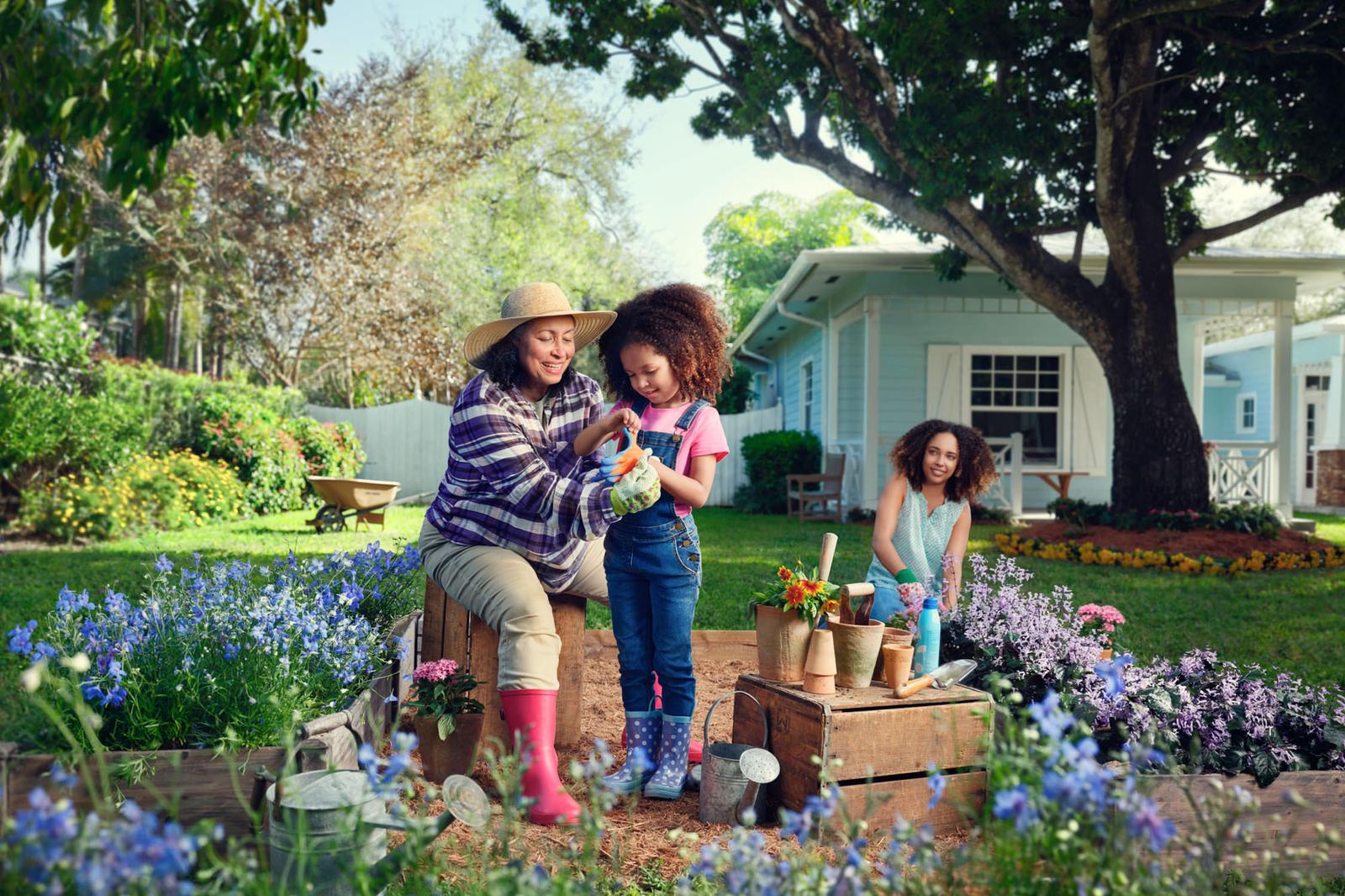 A woman and a young girl sit on a wooden bench in a garden, surrounded by flowers.