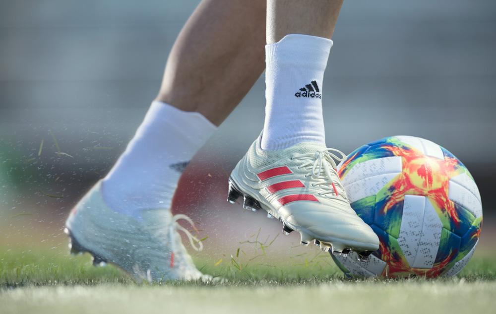A person's legs in football boots kicking a football on a grassy field.