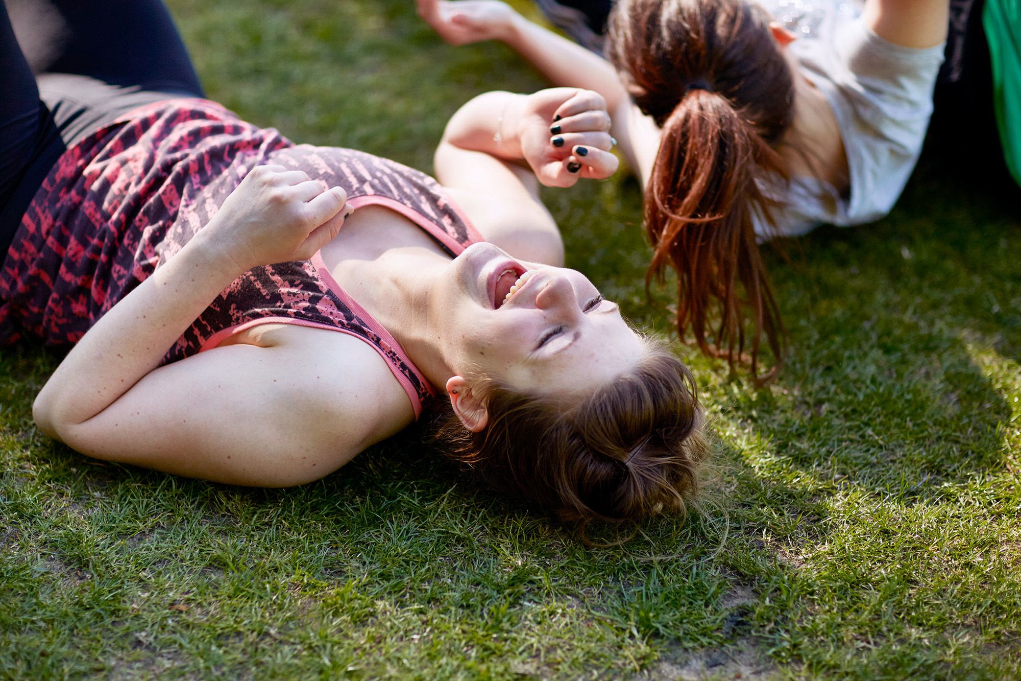 A woman is lying on her back in a field of grass, laughing and smiling.