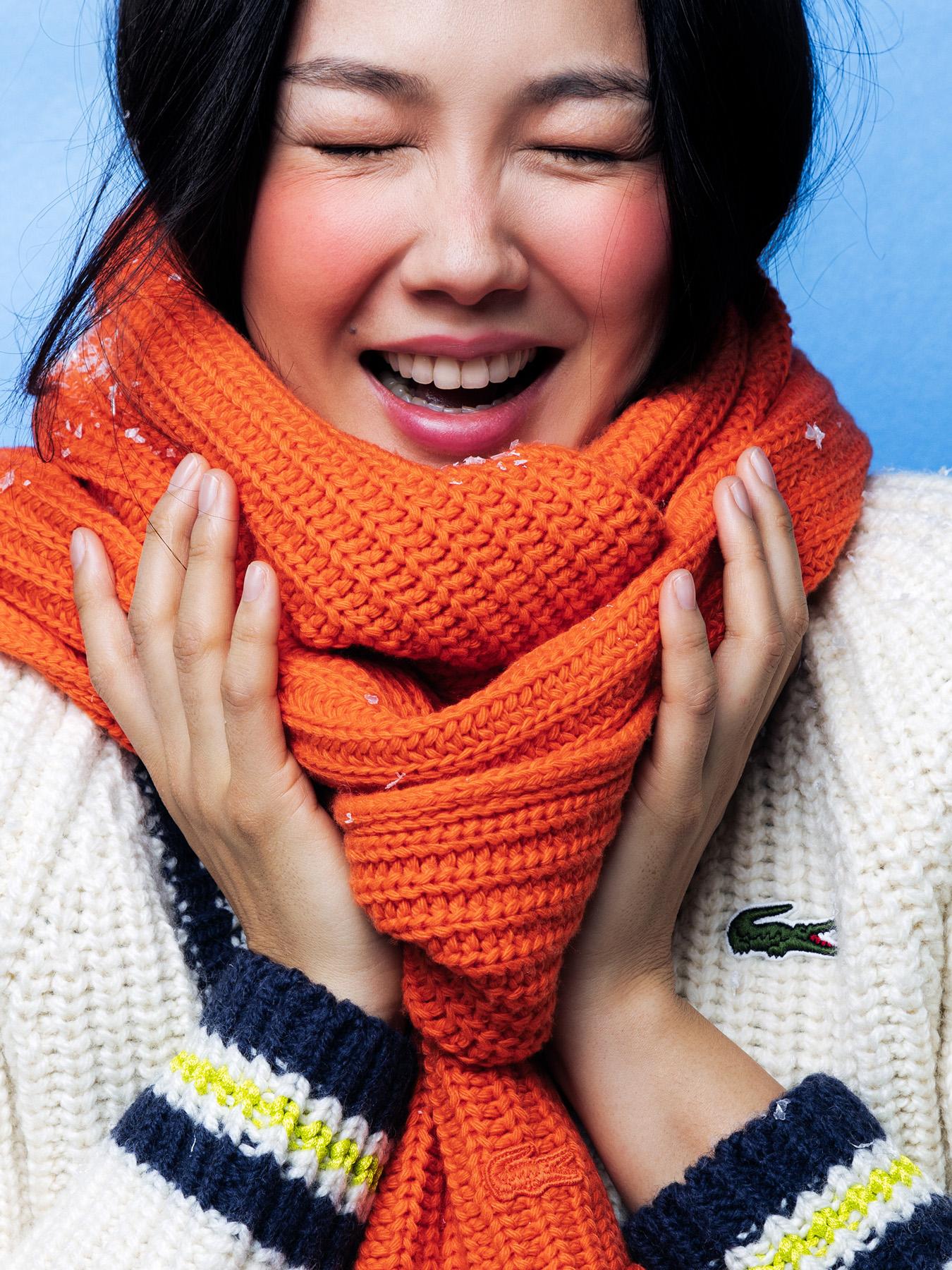 A woman wearing a bright orange scarf and a white sweater, smiling and looking directly at the camera.
