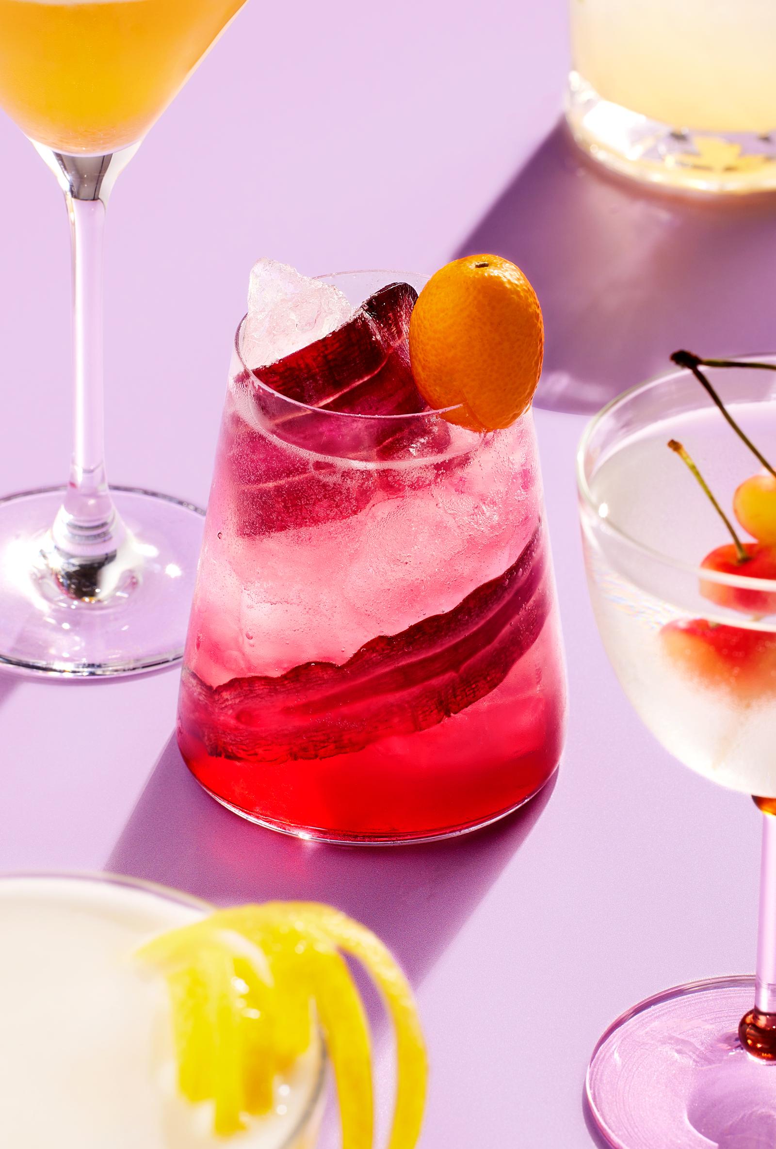 A selection of cocktails in different glasses, featuring a pink drink with a lemon slice and another with a cherry.
