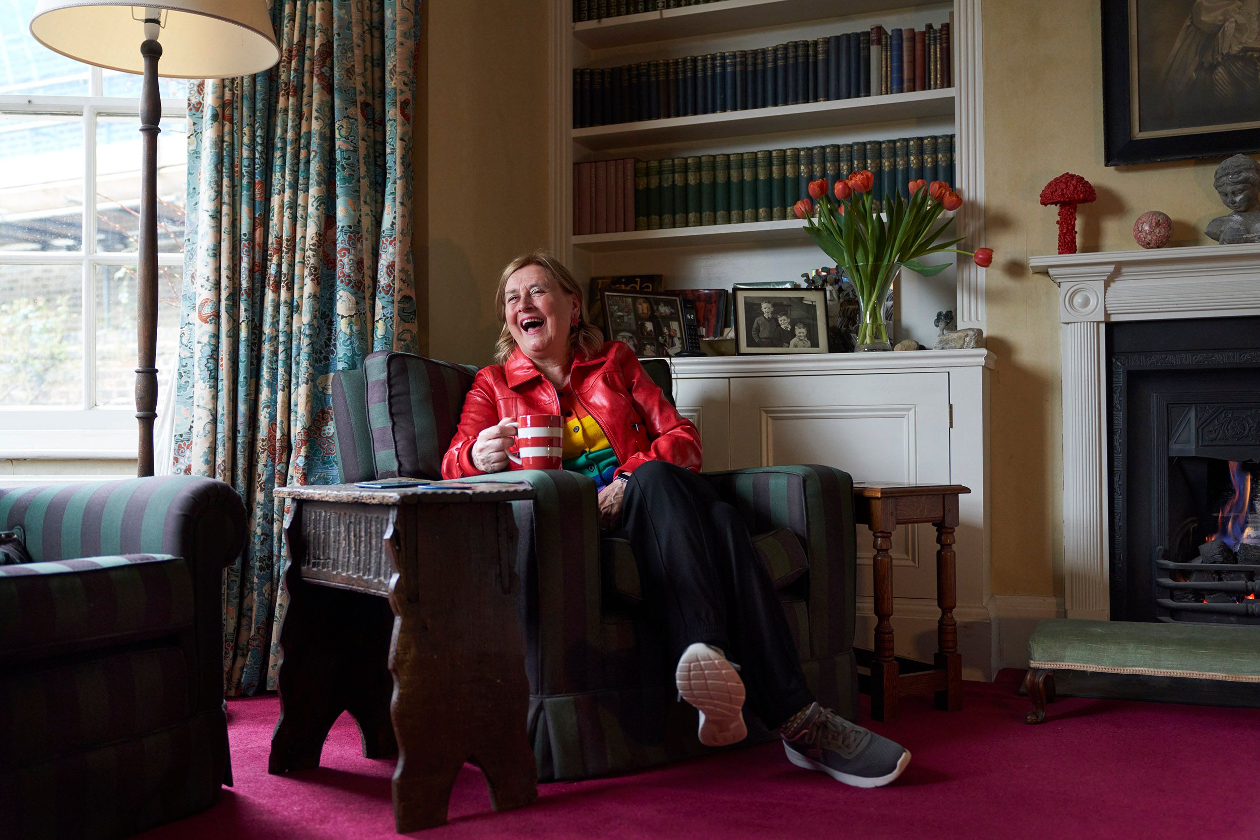 A woman sits in a chair, laughing and holding a cup.