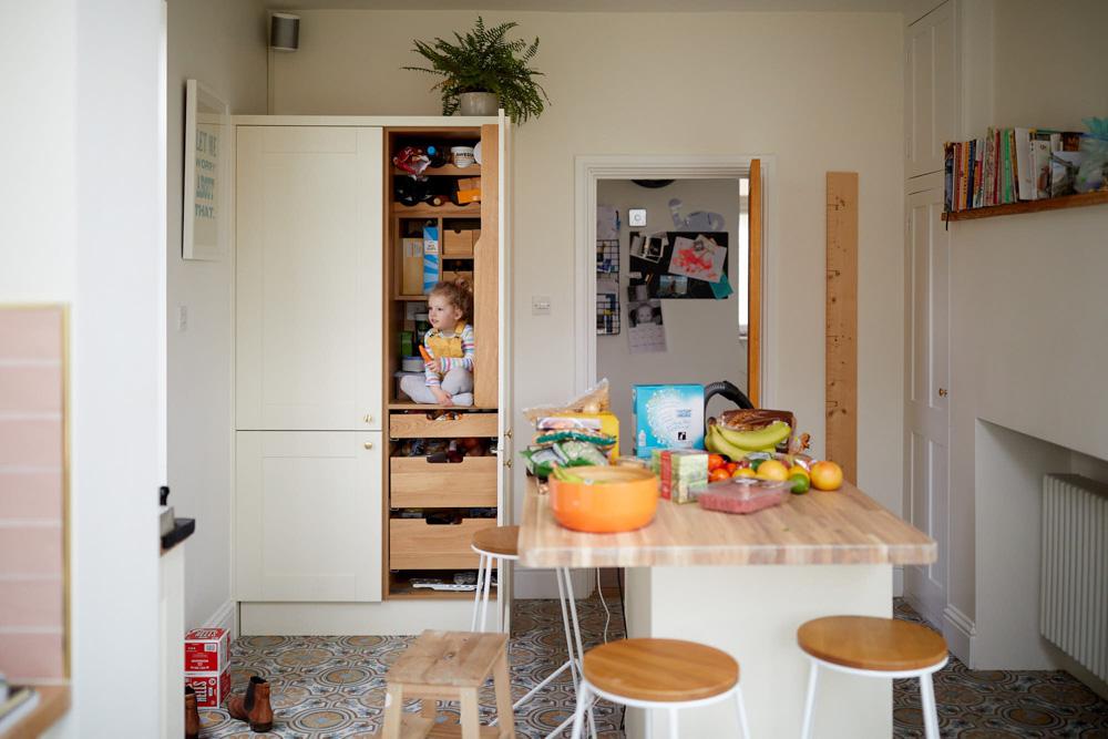 A child sits in a tall, white, wood-lined cupboard, eating a snack. The child's face is focused on the food, and they seem to be enjoying it.
