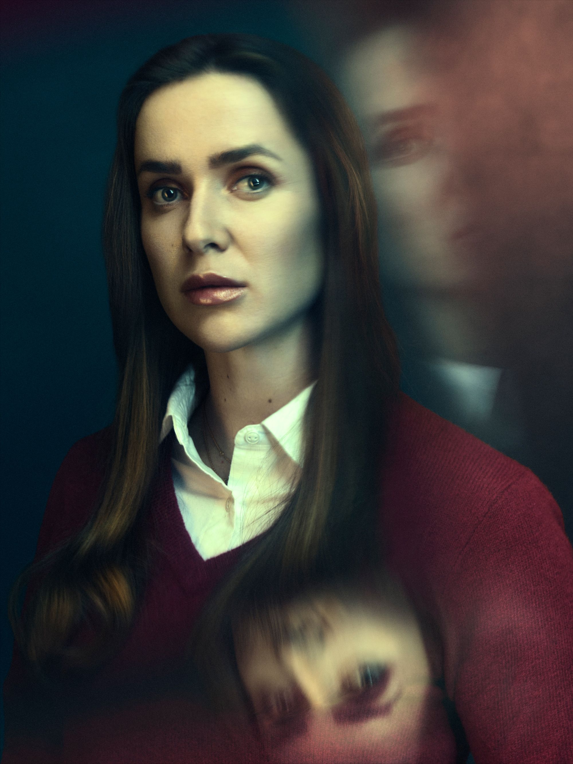 A woman with long brown hair and a red sweater, looking directly at the camera with a serious expression.
