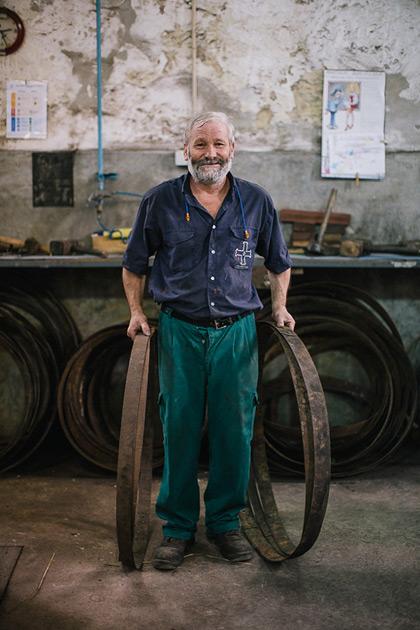 A man with a beard and a blue shirt, holding a large metal ring, in a workshop or factory setting.
