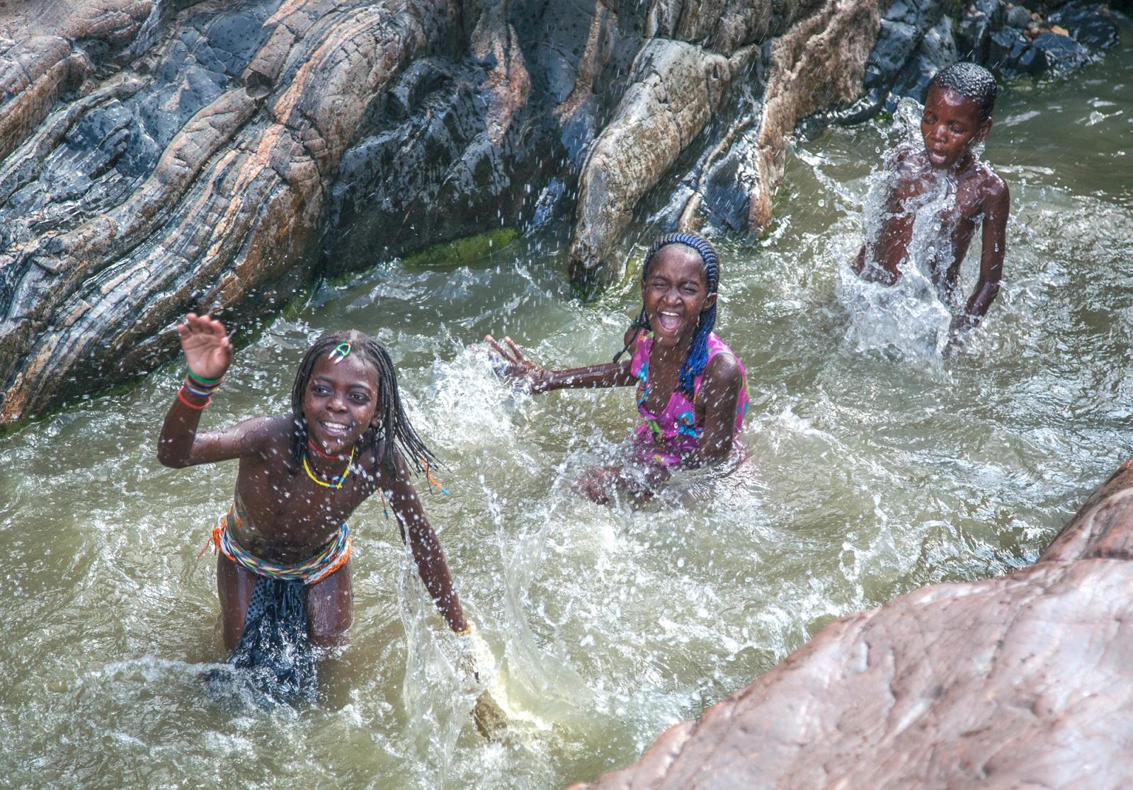Three children play in a rock pool, surrounded by water and rocks.
