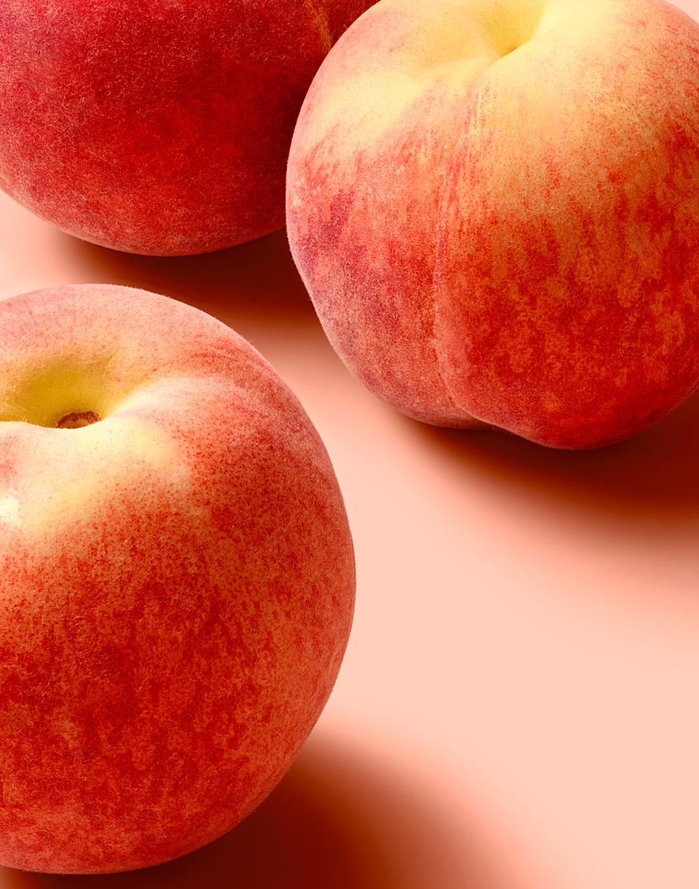 A still life of three ripe, red and yellow peaches.