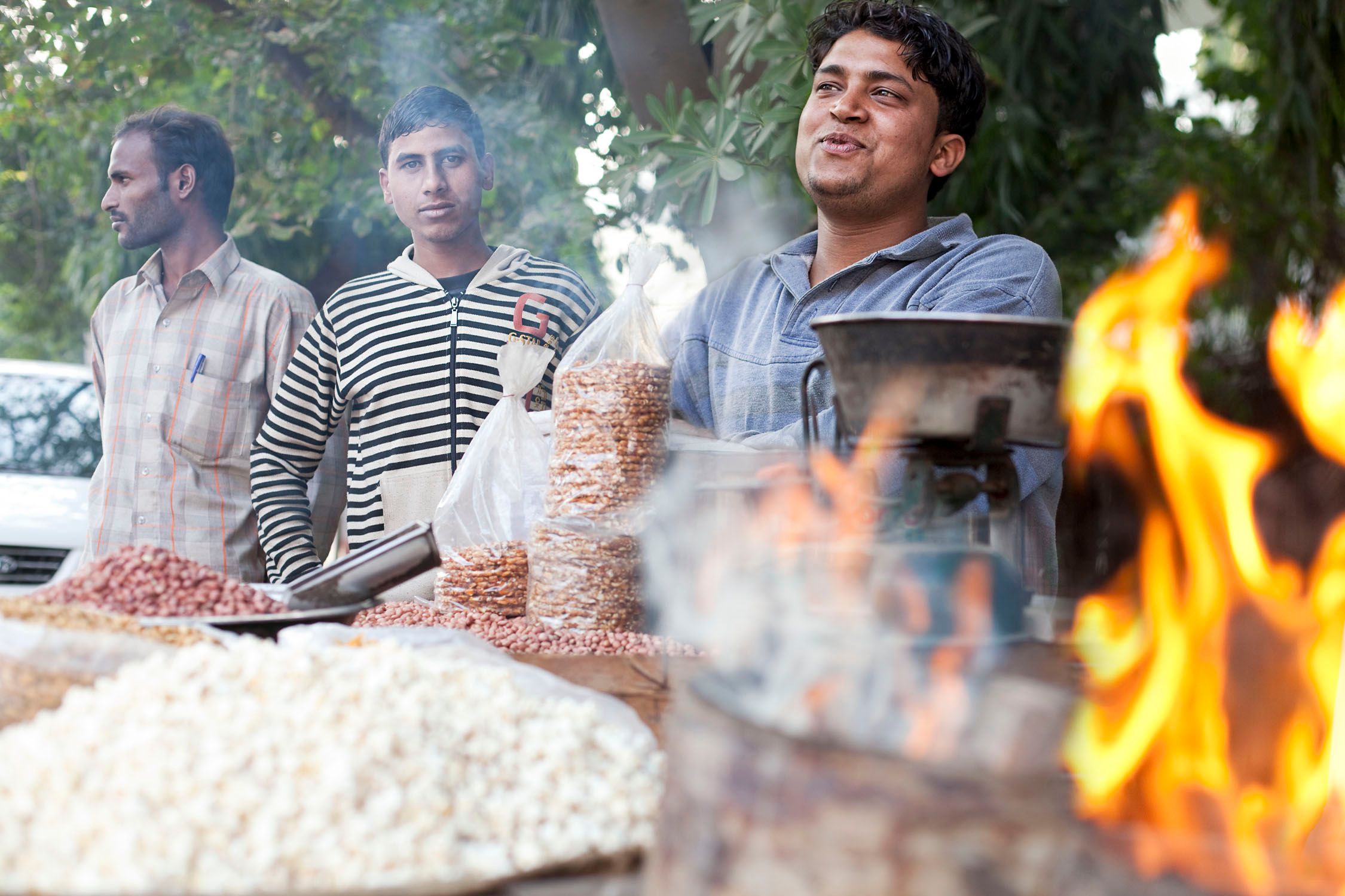 A street vendor selling snacks with a large pot on fire in the foreground.