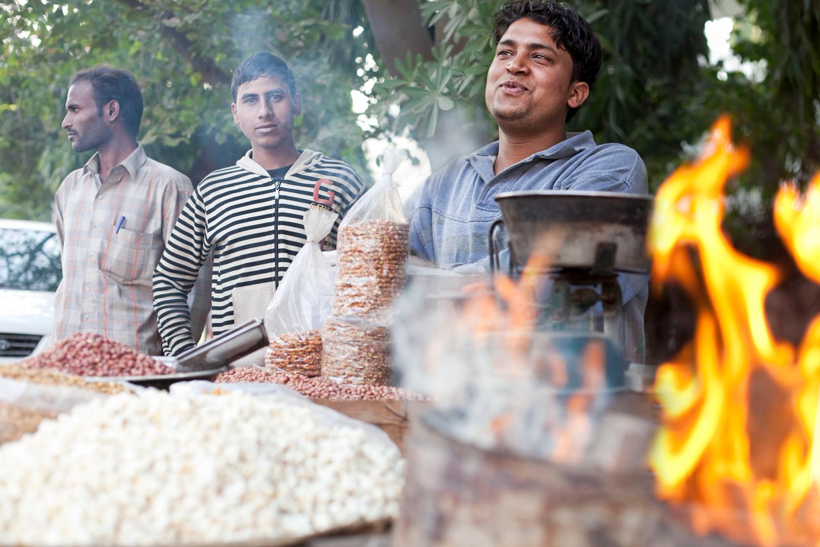 A street vendor selling snacks with a large pot on fire in the foreground.