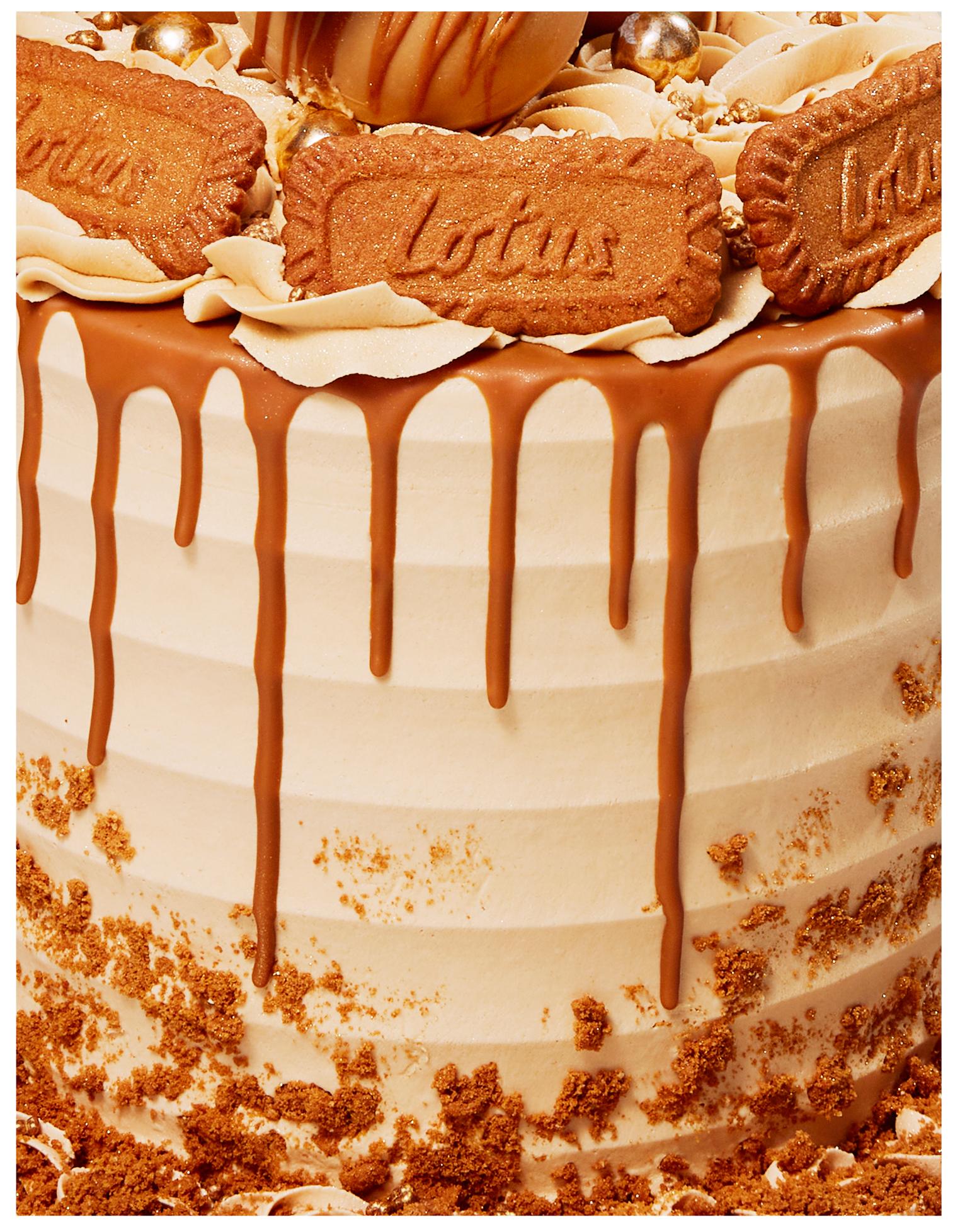 This image is a close-up of a large, multi-layered cake with a light brown frosting and a caramel drizzle. The cake is covered in a light brown frosting and has a caramel drizzle.