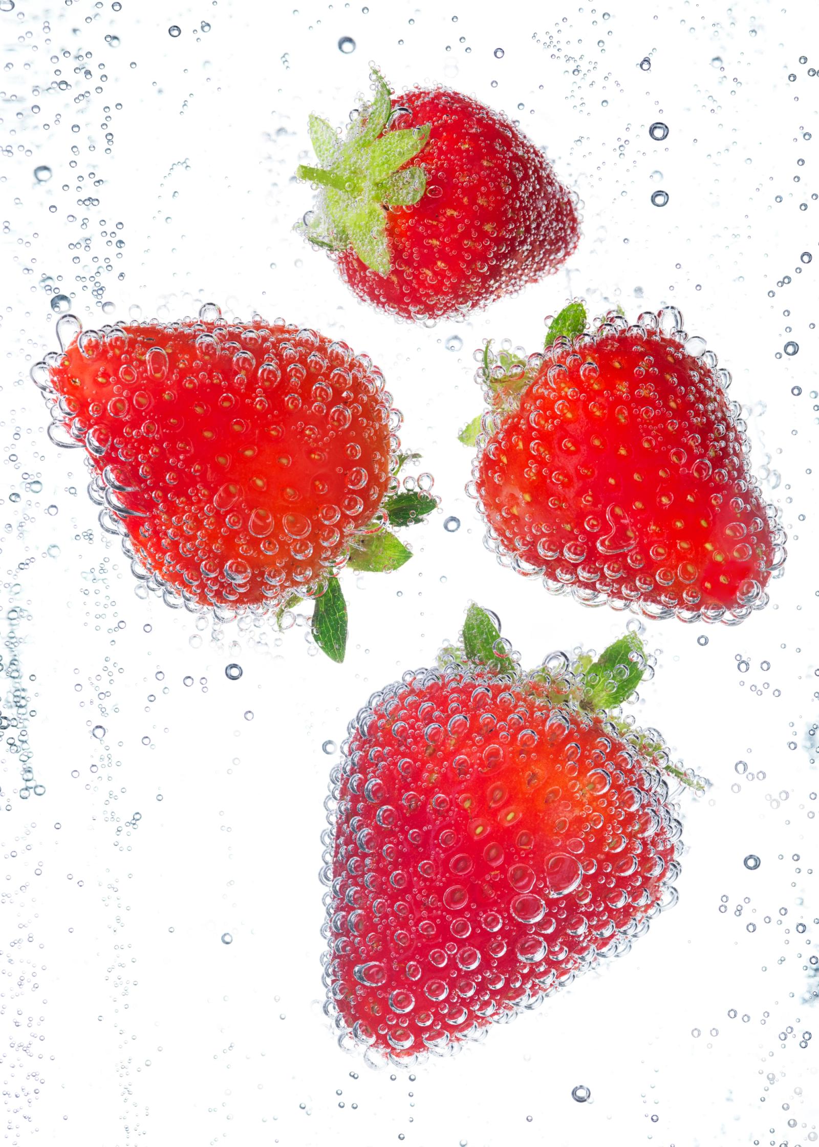 A close-up of several strawberries in a glass of water, surrounded by bubbles.
