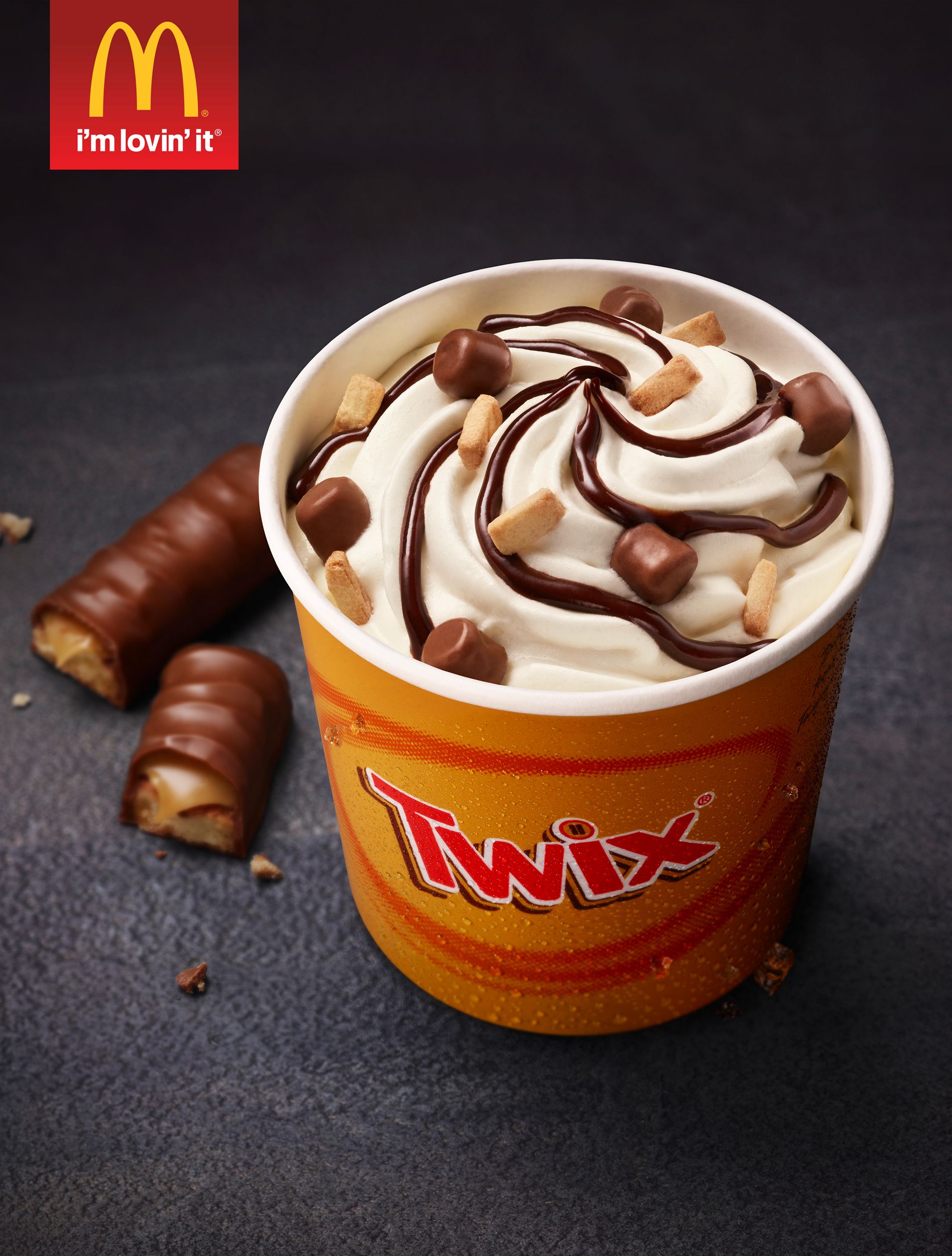A McDonald's McFlurry with Twix-flavored mix-ins, topped with whipped cream and chocolate sauce, in a yellow and red Twix-branded cup.