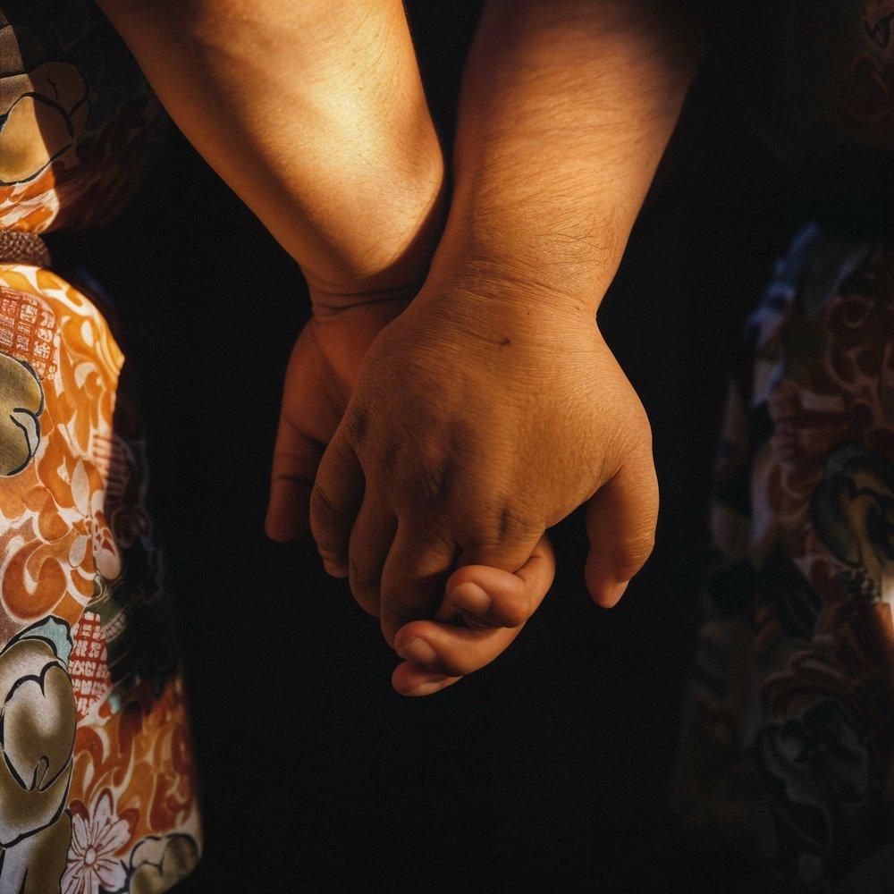 Two people hold hands with intertwined arms and fingers.