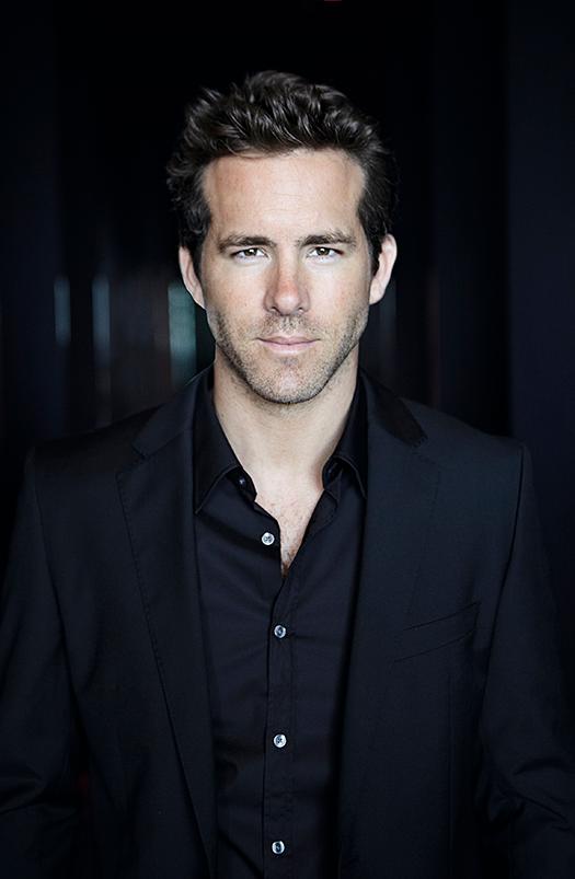 A man in a black suit and black shirt, with a hint of a sports-related background in the background.