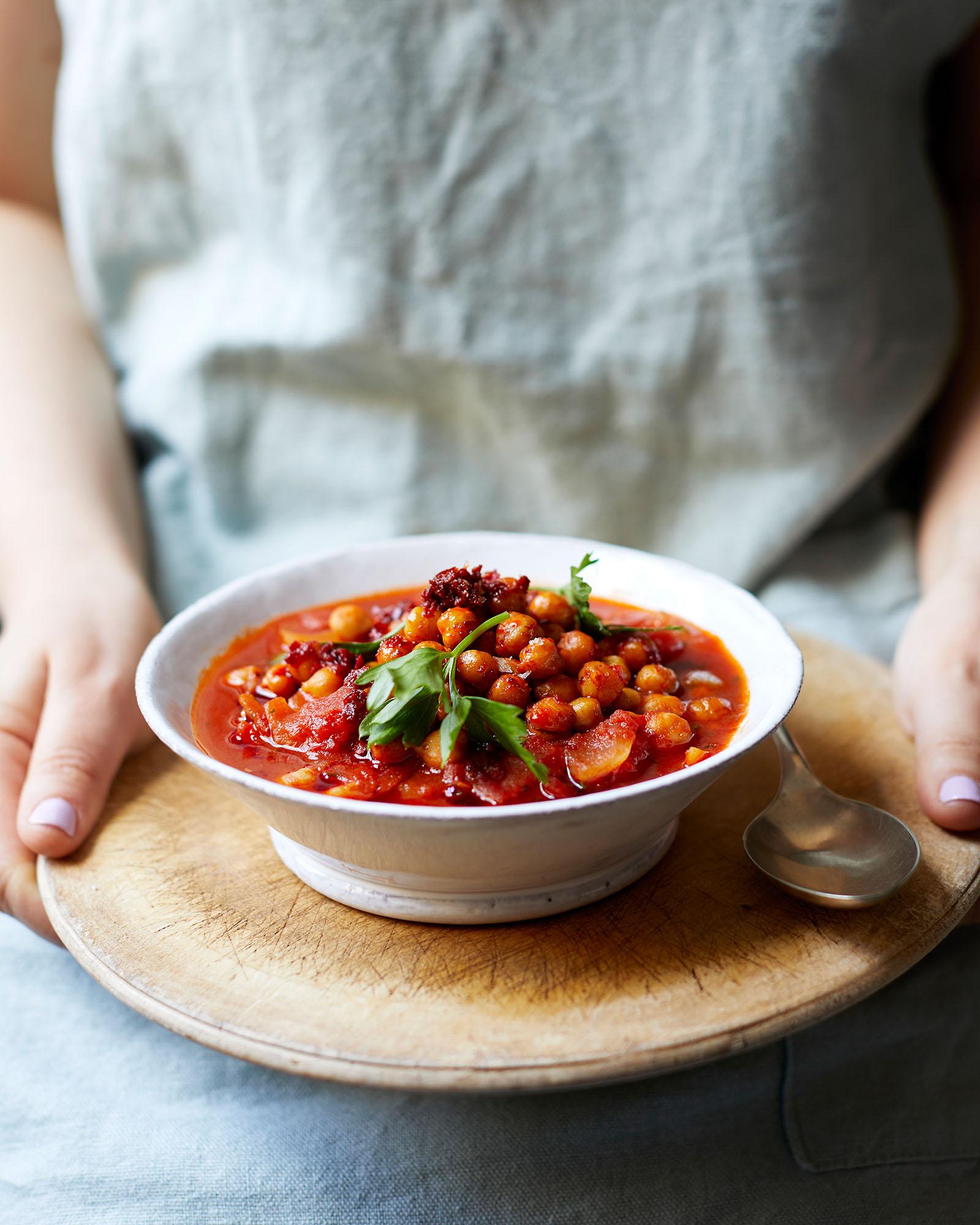 A bowl of stew or soup, possibly a tomato-based soup with chickpeas, garnished with fresh herbs.
