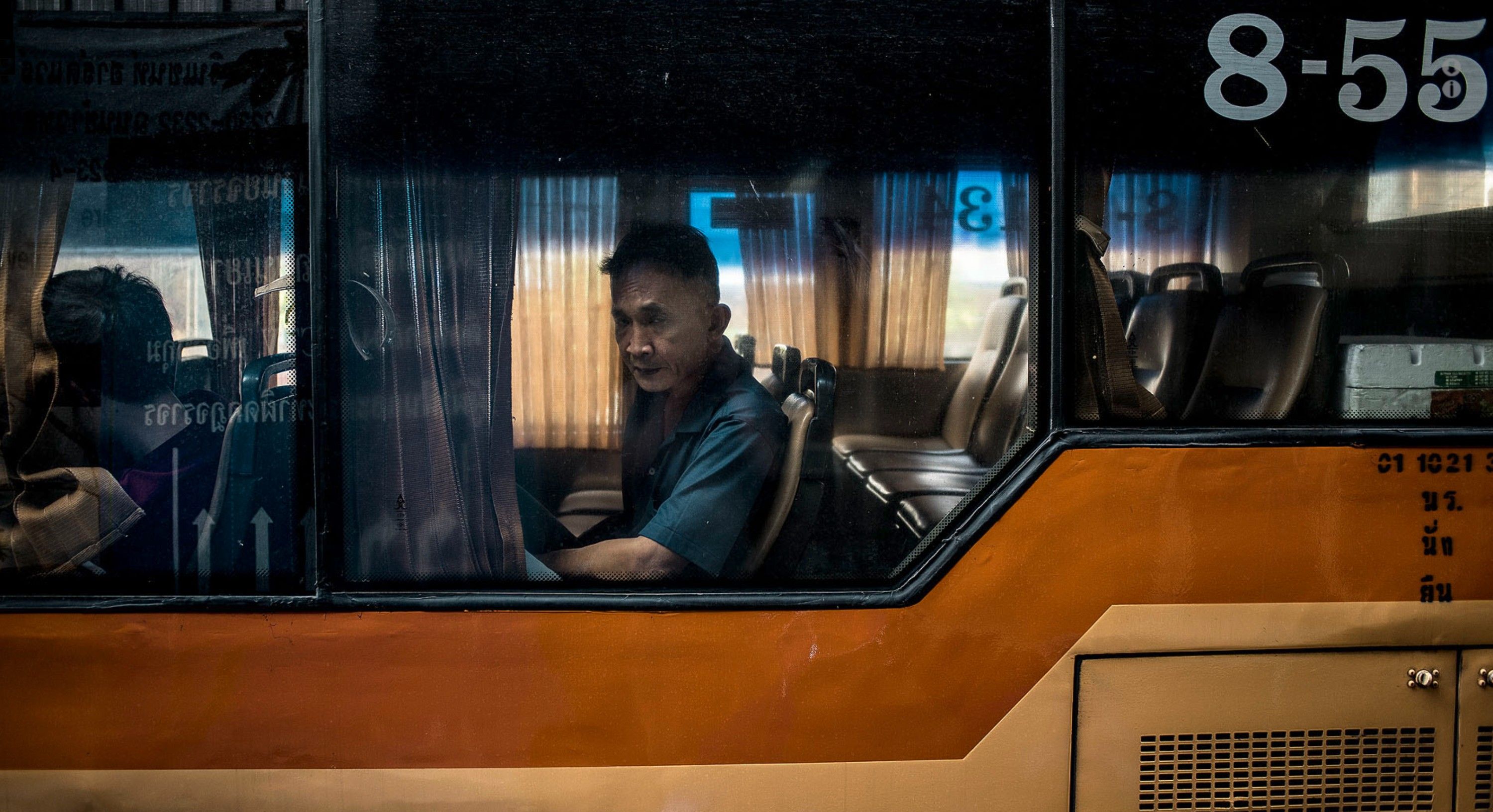 A man in a blue shirt is sitting in a bus, looking out the window at an urban cityscape.
