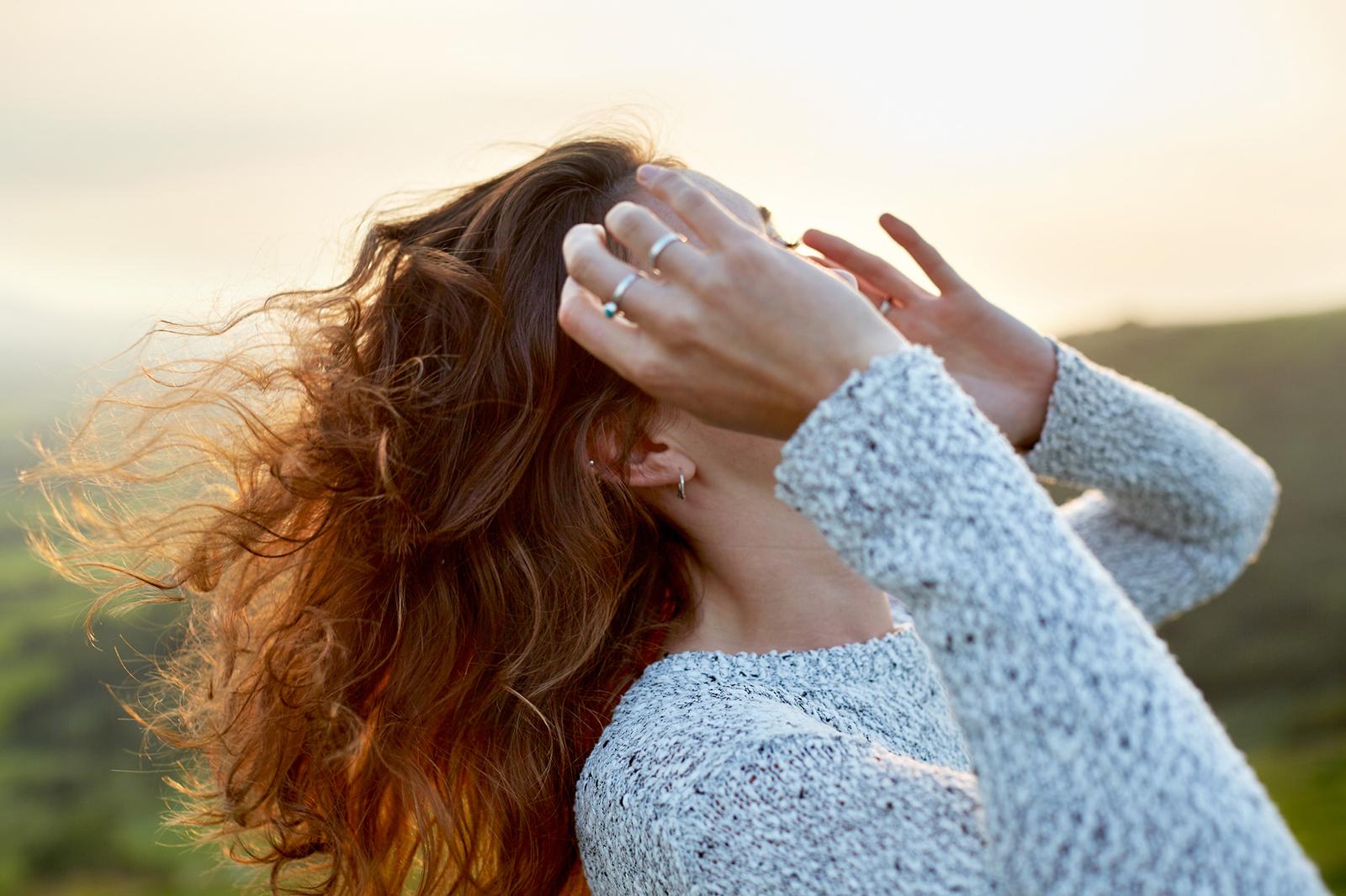A woman with long, flowing hair is running her fingers through it, with the wind blowing it in every direction.