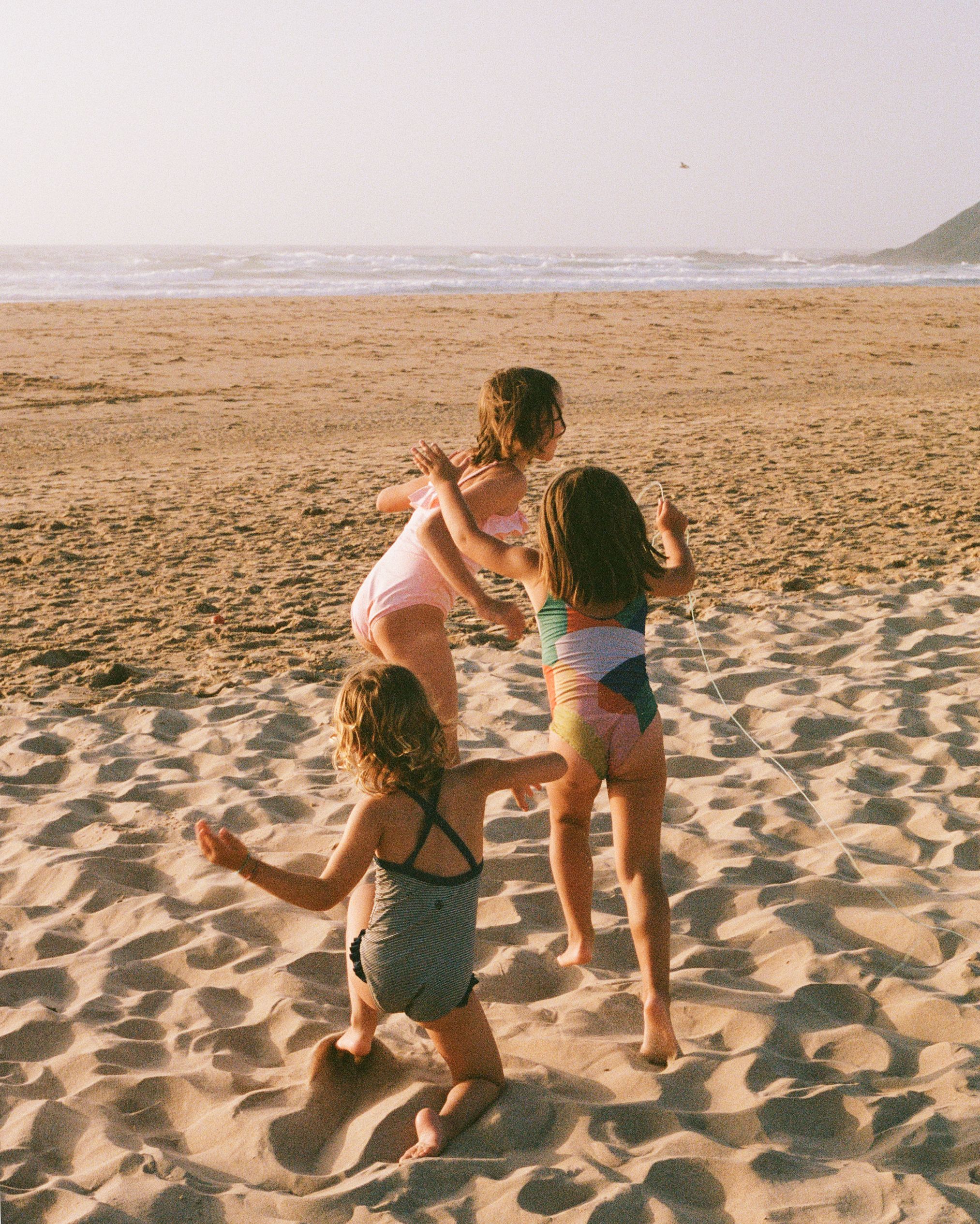 Three girls in swimsuits playing on a beach.