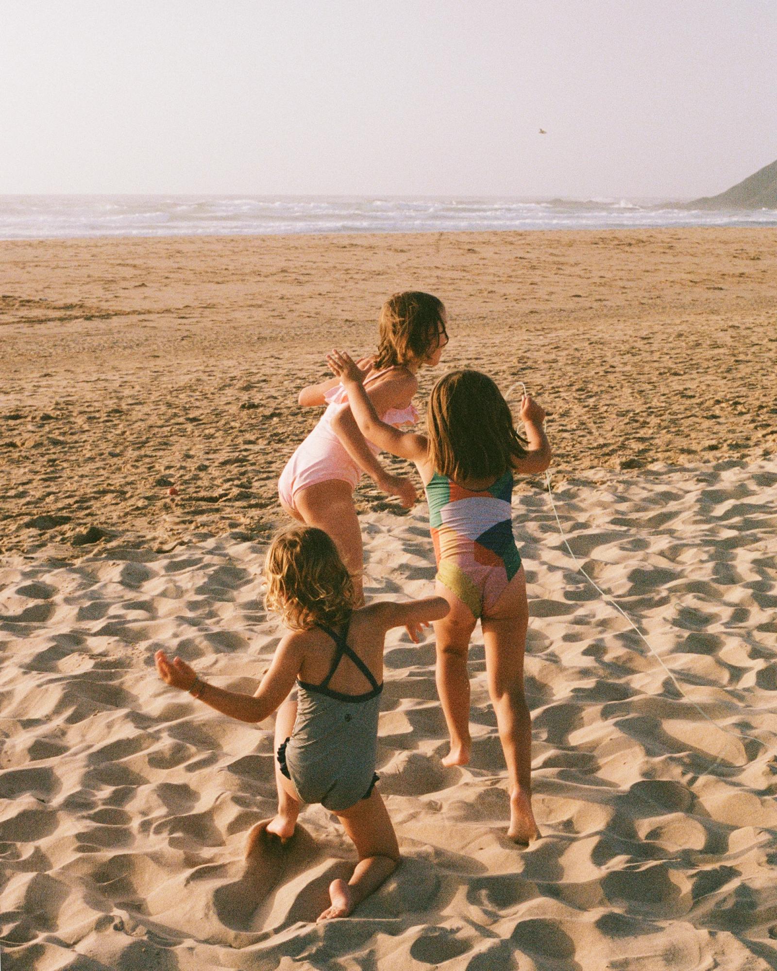 Three girls in swimsuits playing on a beach.