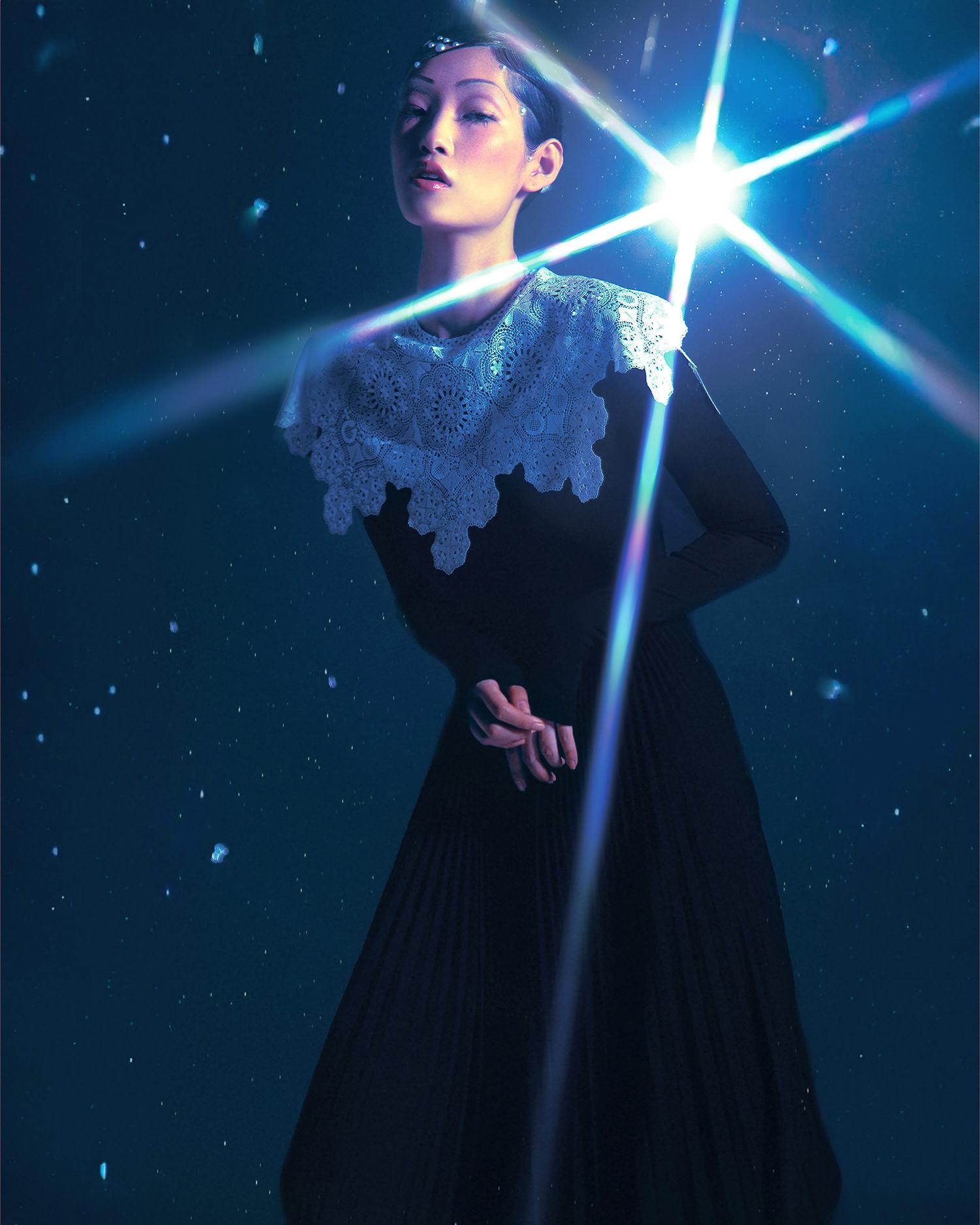 A woman in a black dress with a white lace collar, posing in a dark, starry environment with a bright, shining light in the background.