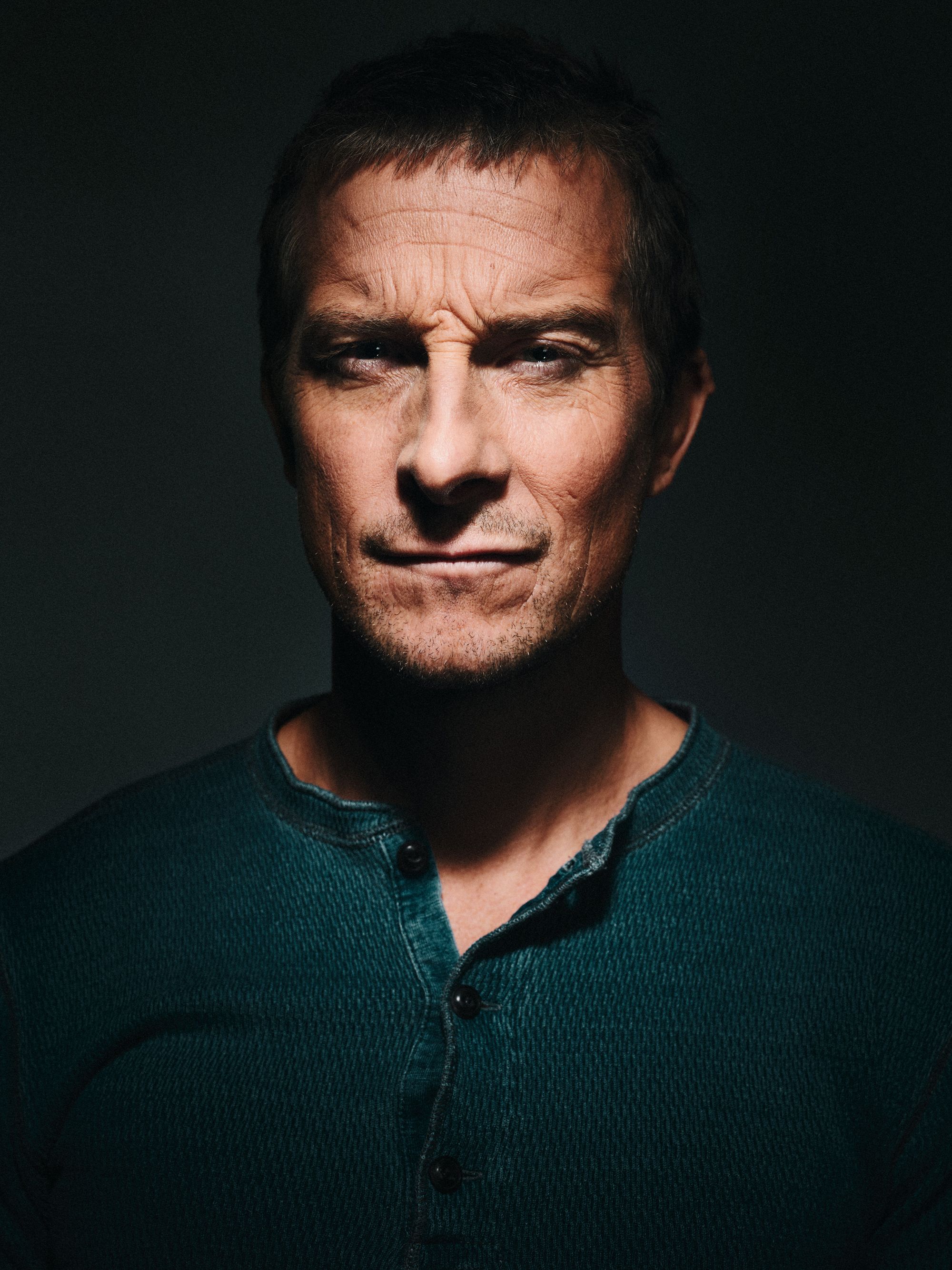 A man with a serious expression, wearing a dark green sweater with a subtle texture.