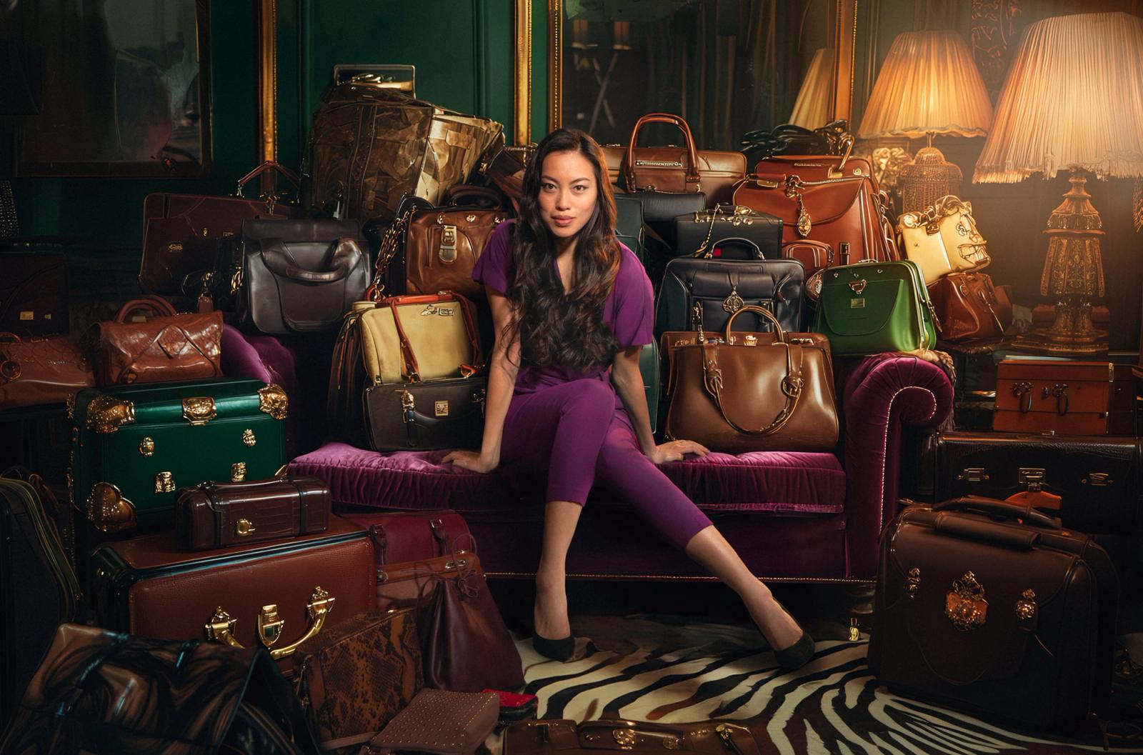 A woman sits on a couch surrounded by handbags and luggage.