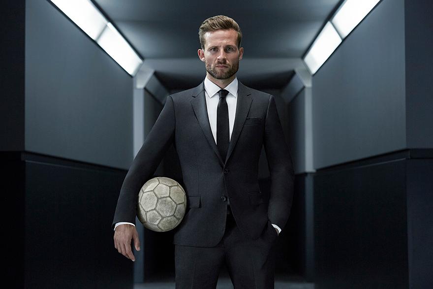 David Beckham holds a soccer ball in a black suit.