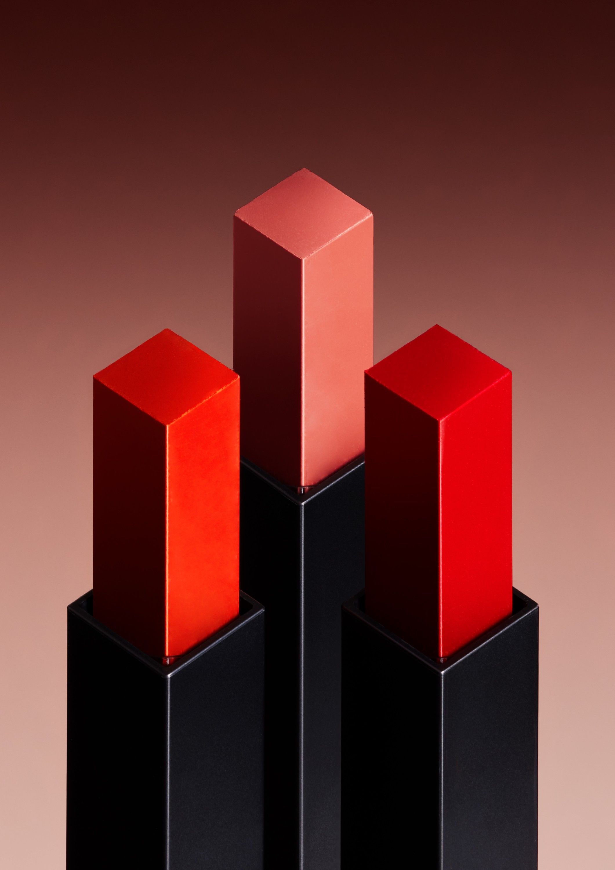 A collection of lipstick tubes in various shades of red and pink, arranged in a pyramid-like structure.
