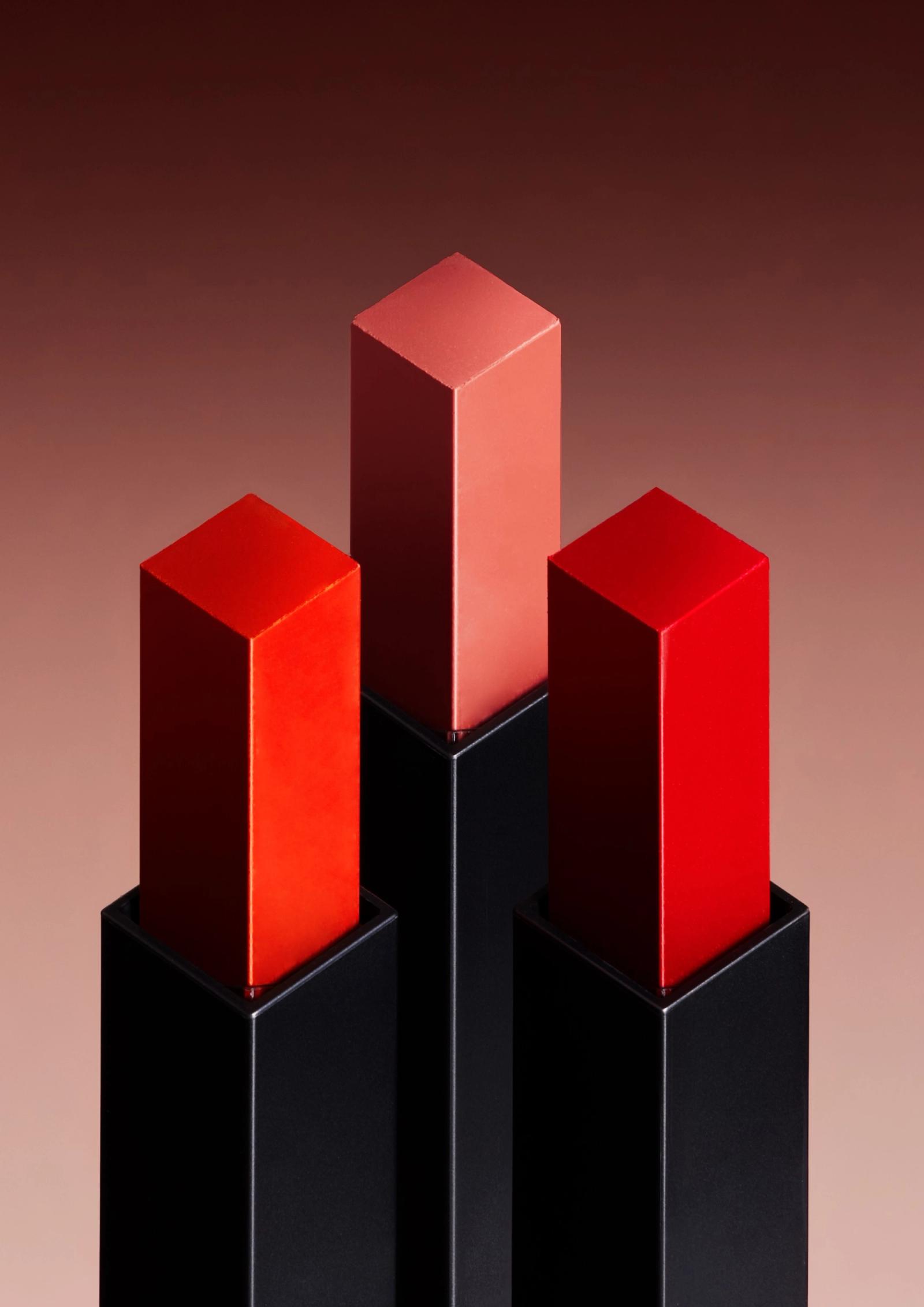 A collection of lipstick tubes in various shades of red and pink, arranged in a pyramid-like structure.