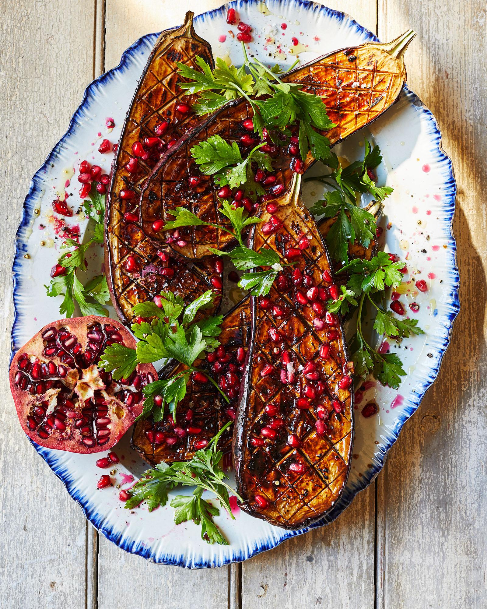 A plate featuring roasted eggplant, pomegranate seeds, and parsley.