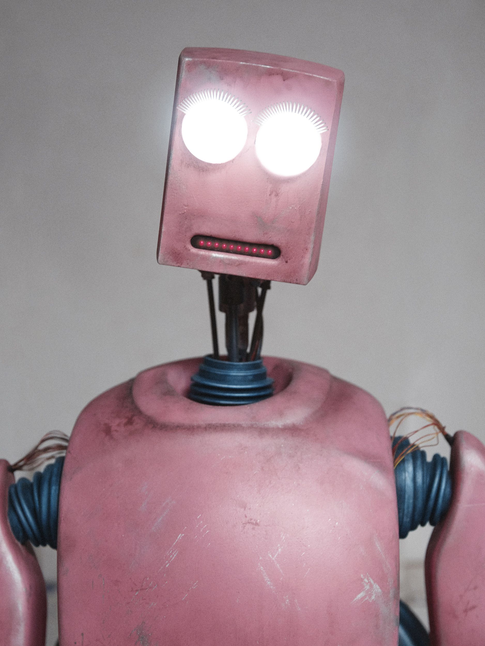 A pink, distressed robot-like figure with a square head and glowing eyes, wearing a metallic, industrial-style full-body suit.