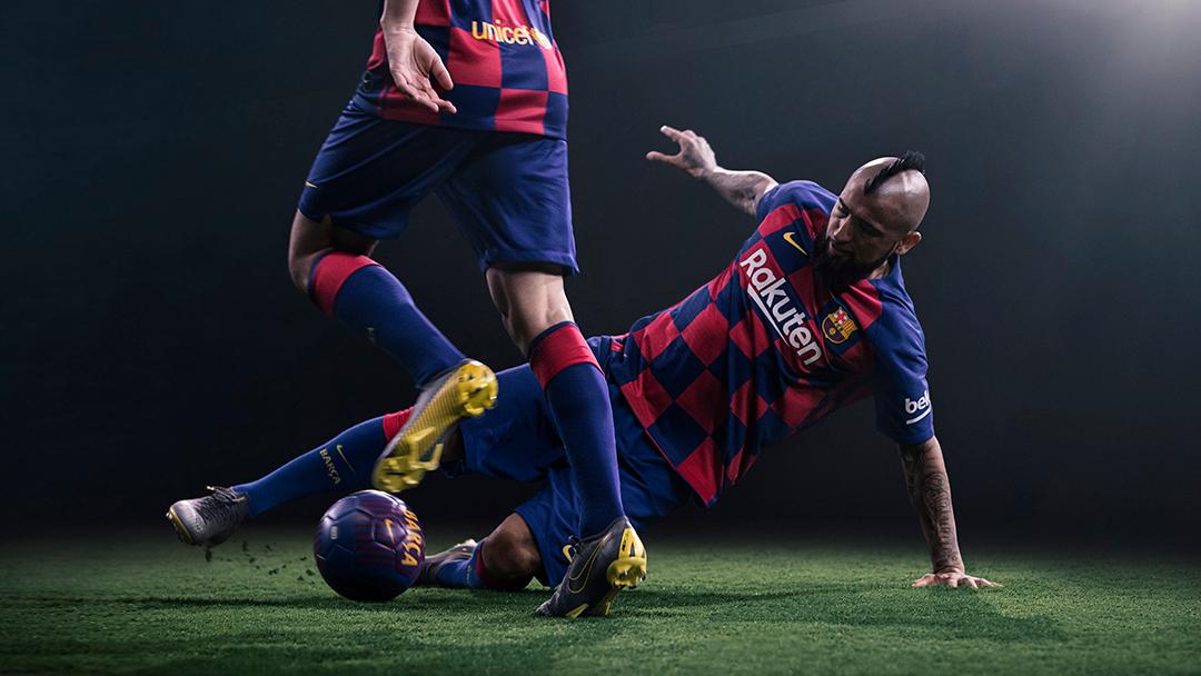 A soccer player in a red and blue jersey, with a football at his feet, on a green grassy field.