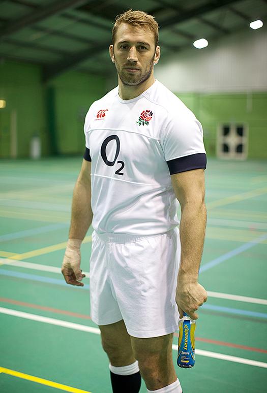 A man wearing a white rugby jersey with a red rose logo, holding a rugby ball.