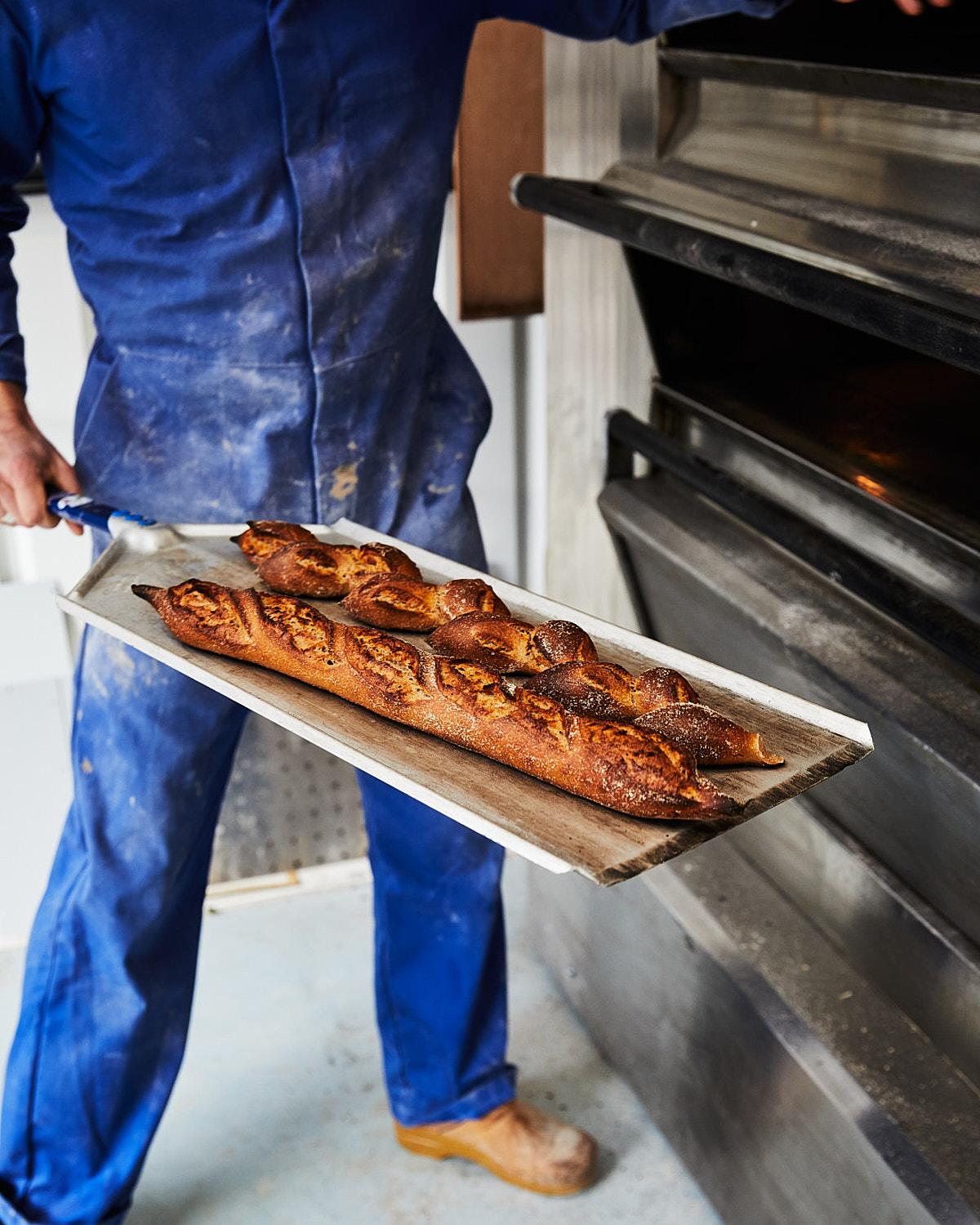 A person holds a tray of freshly baked bread.