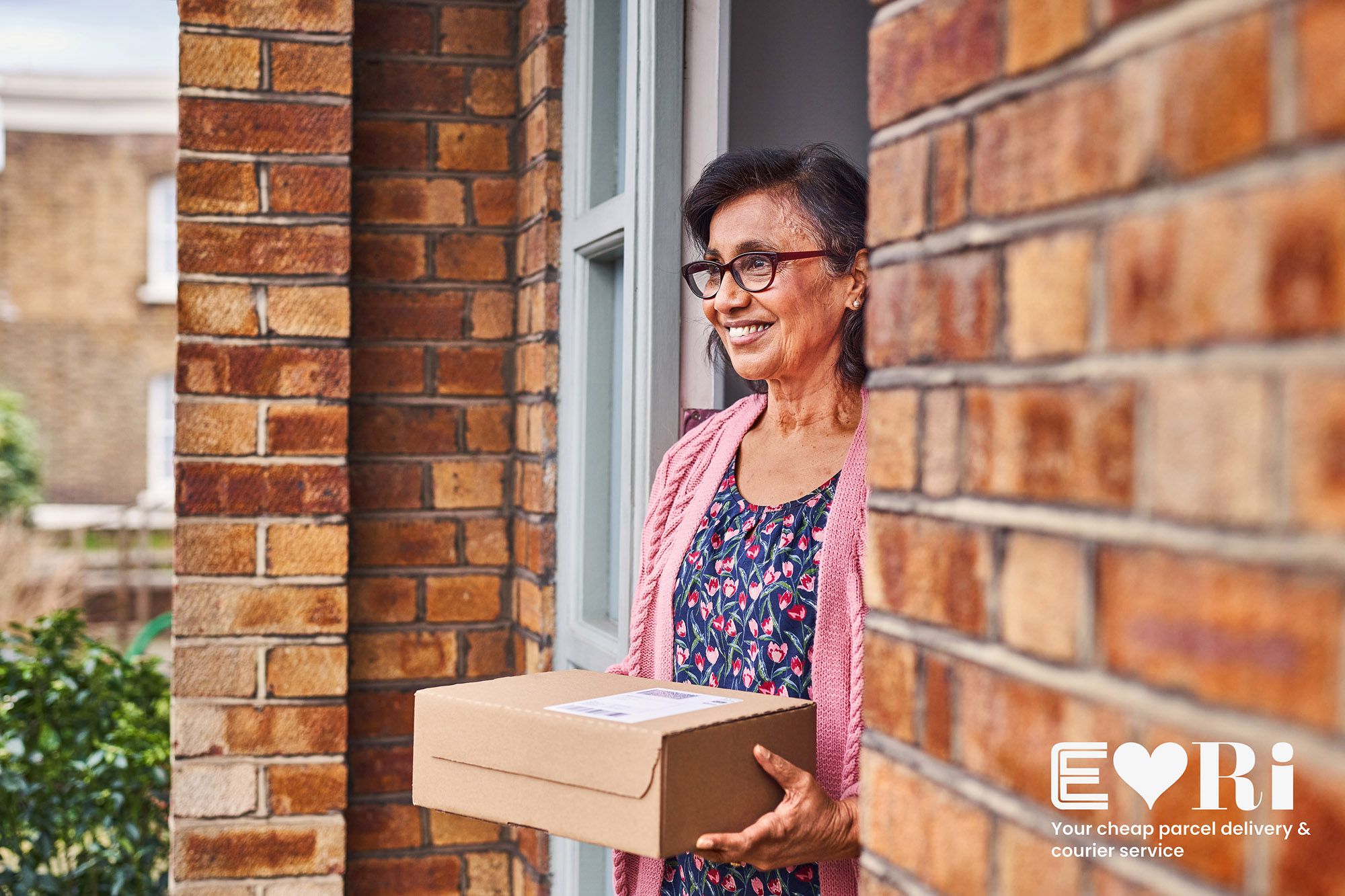 A woman holds a cardboard box at a front door.