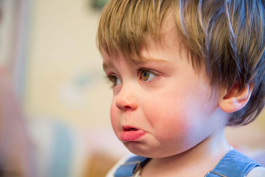 A young boy with a distressed expression, wearing a blue and white striped shirt, looking directly at the camera with a mix of anger and sadness in his eyes.