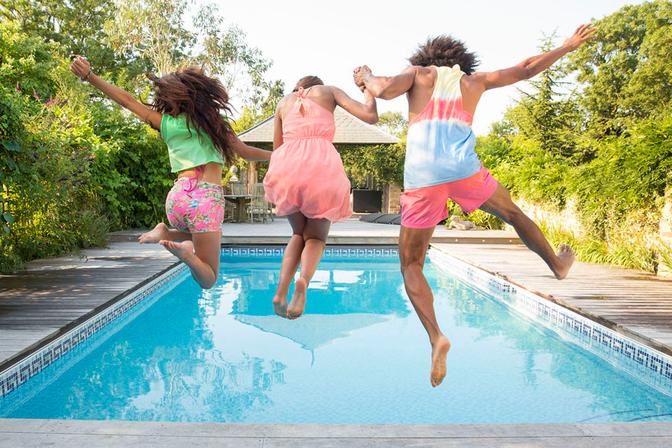 Three people, two women and one man, jumping into a swimming pool, wearing swimsuits and sunglasses.