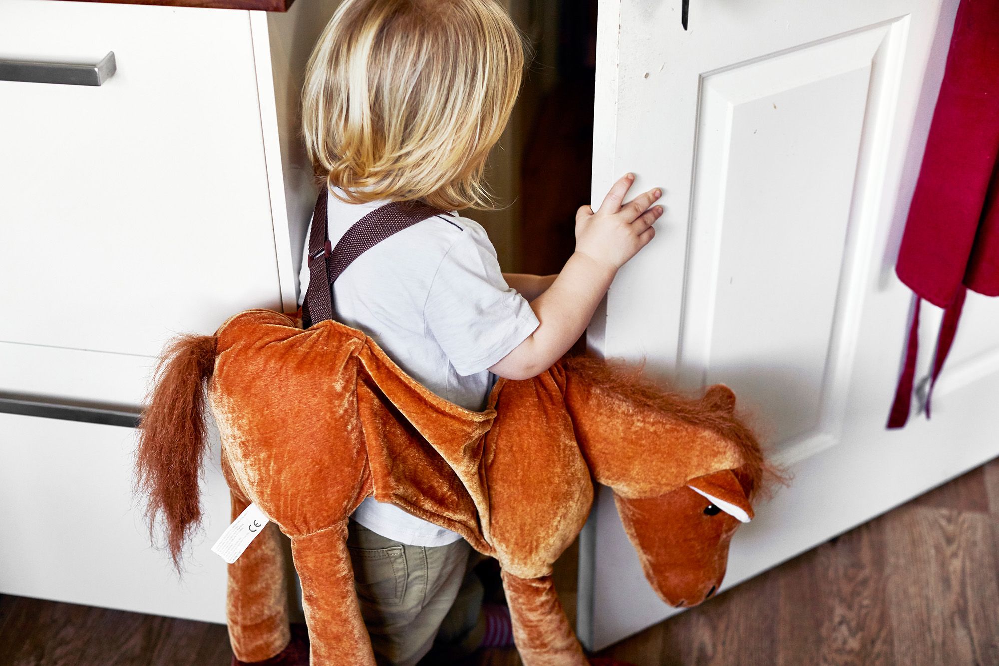 A toddler in a large plush horse costume standing in front of a white door.