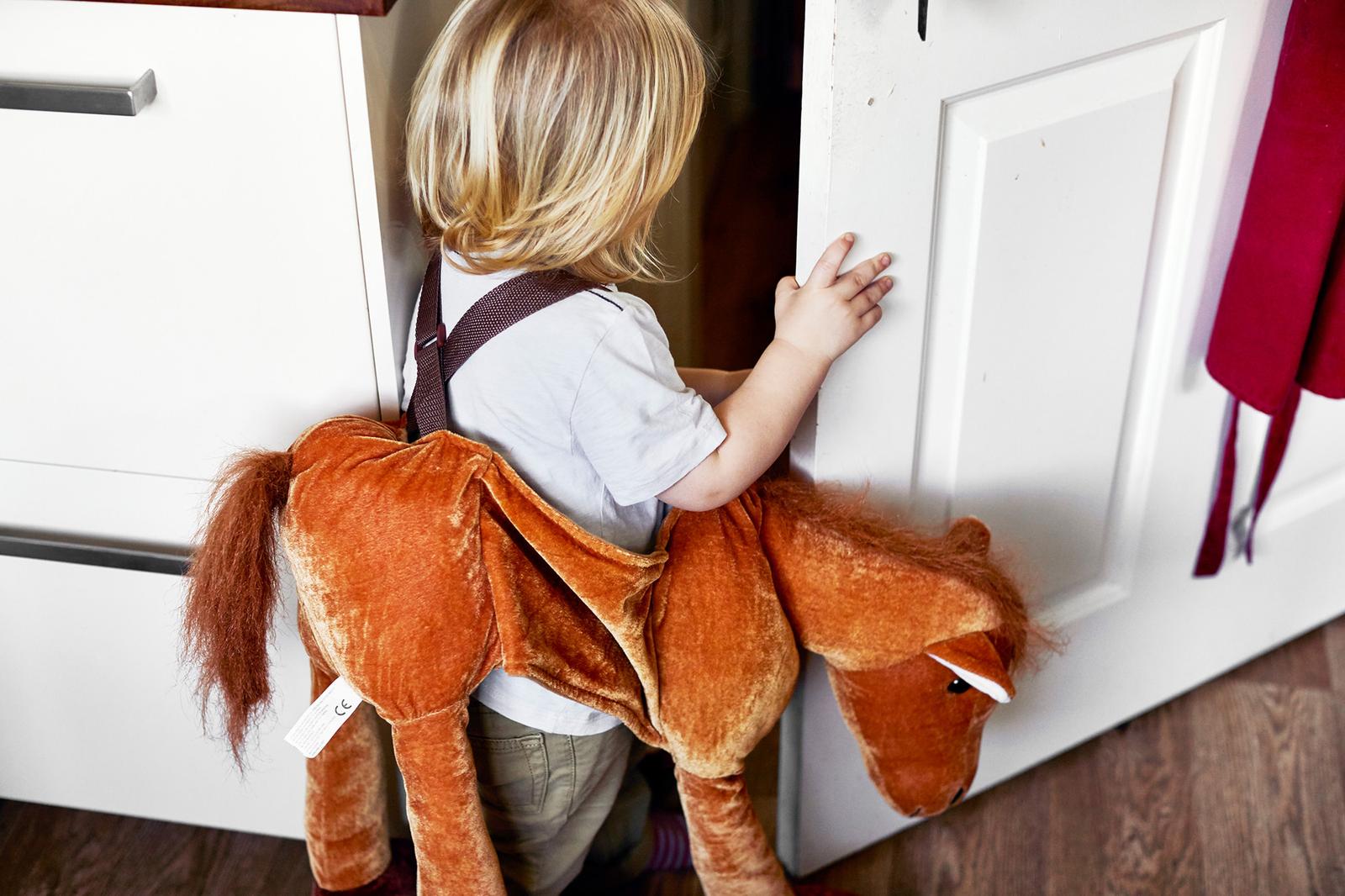 A toddler in a large plush horse costume standing in front of a white door.