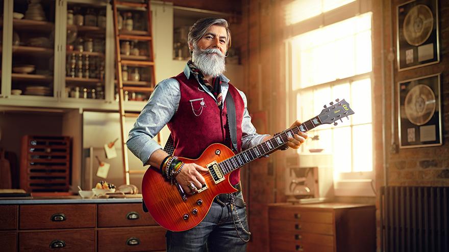 A man in a red vest playing a guitar in a studio.