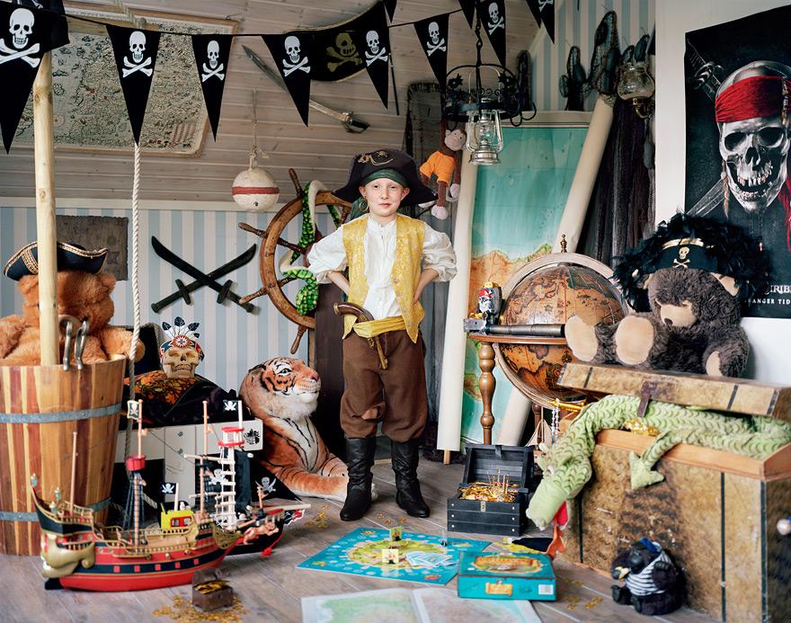 A young boy dressed as a pirate, surrounded by pirate-themed toys and decorations, including a pirate ship, a tiger, a treasure chest, and a pirate flag.